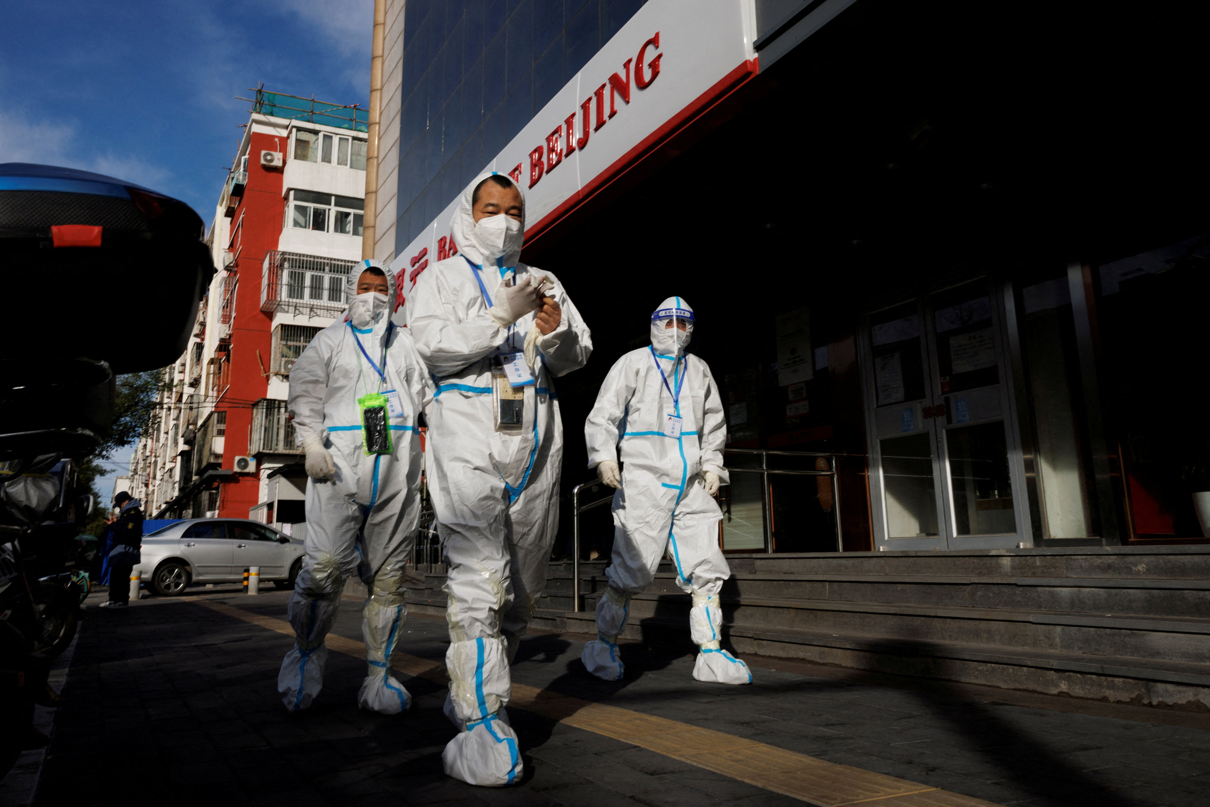 Pandemic-prevention workers walk near a locked-down apartment compound in Beijing on Saturday, a day after the State Council issued 20 measures to ease some coronavirus controls. Photo: Reuters