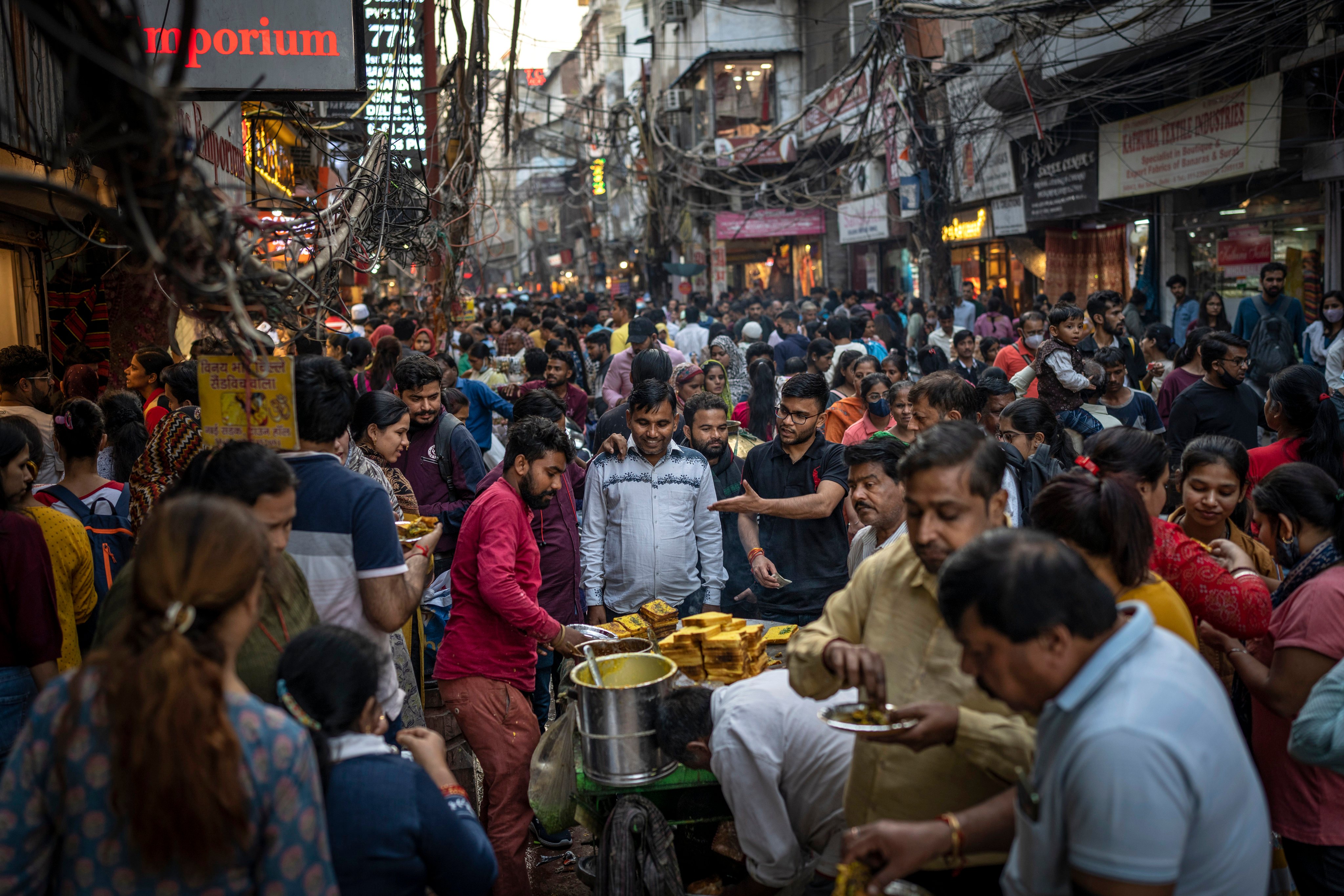 People eat street food as shoppers crowd a market in New Delhi on November 12. India is expected to take over from China as the world’s most populous country in the next few years. Photo: AP