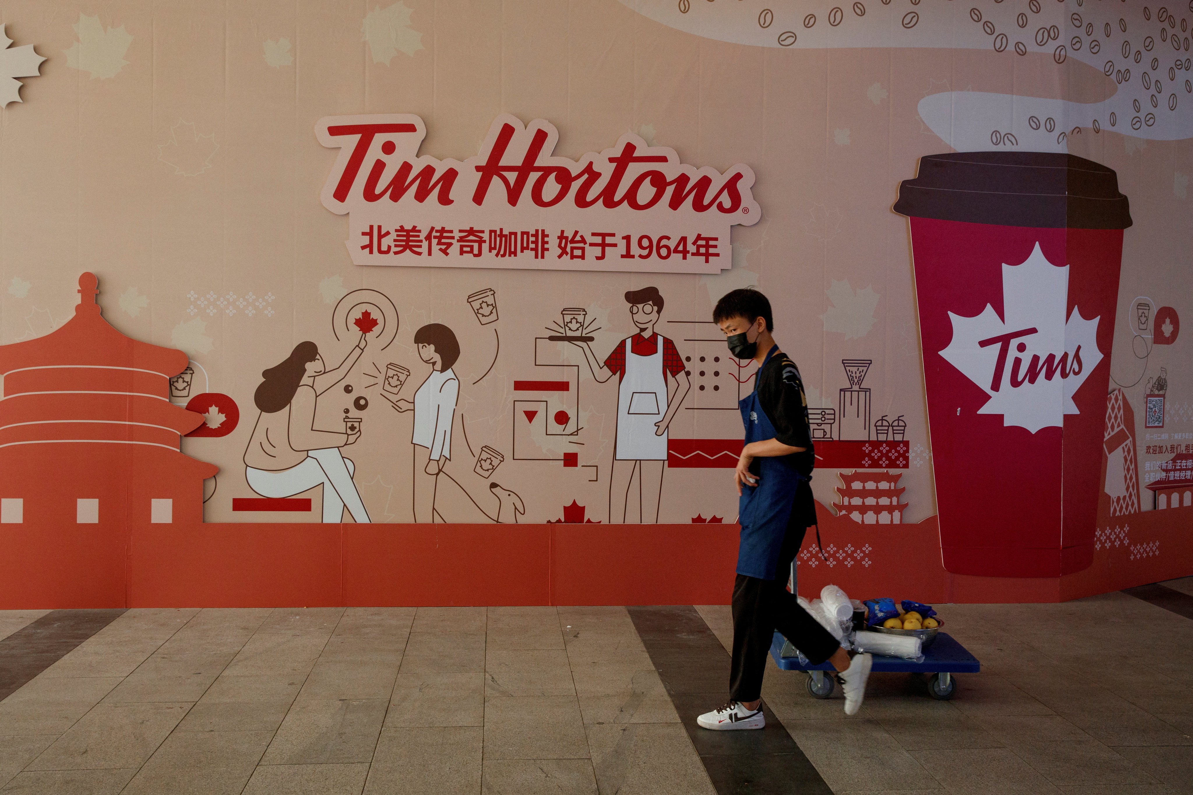 A man walks past a store front poster advertising the opening of a Tim Hortons cafe in Beijing. Photo: Reuters