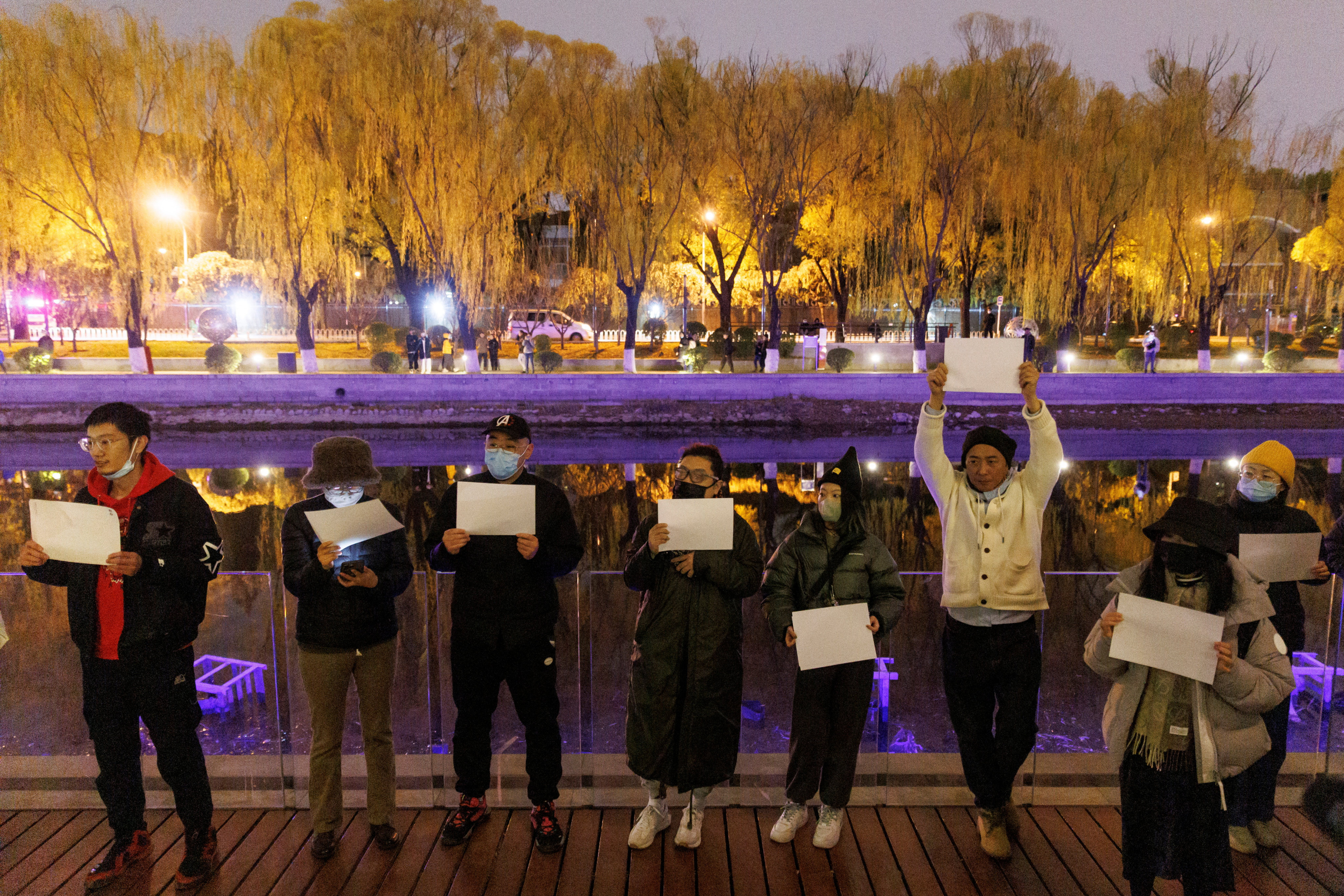 At a vigil in Beijing, people hold white sheets of paper in protest over coronavirus restrictions while commemorating the victims of a fire in Urumqi on Thursday. Photo: Reuters