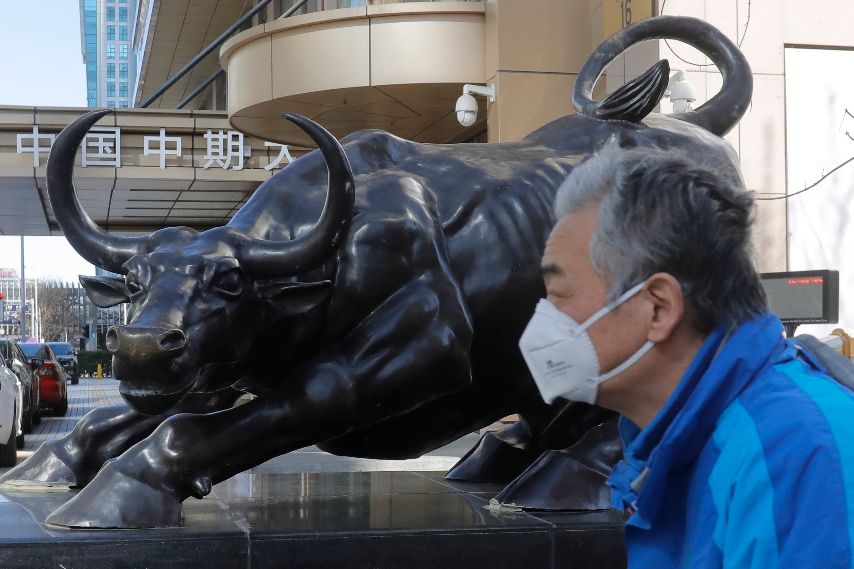 A man walks by a bronze sculpture of a bull in the central business district in Beijing, in March 2020. Photo: EPA-EFE