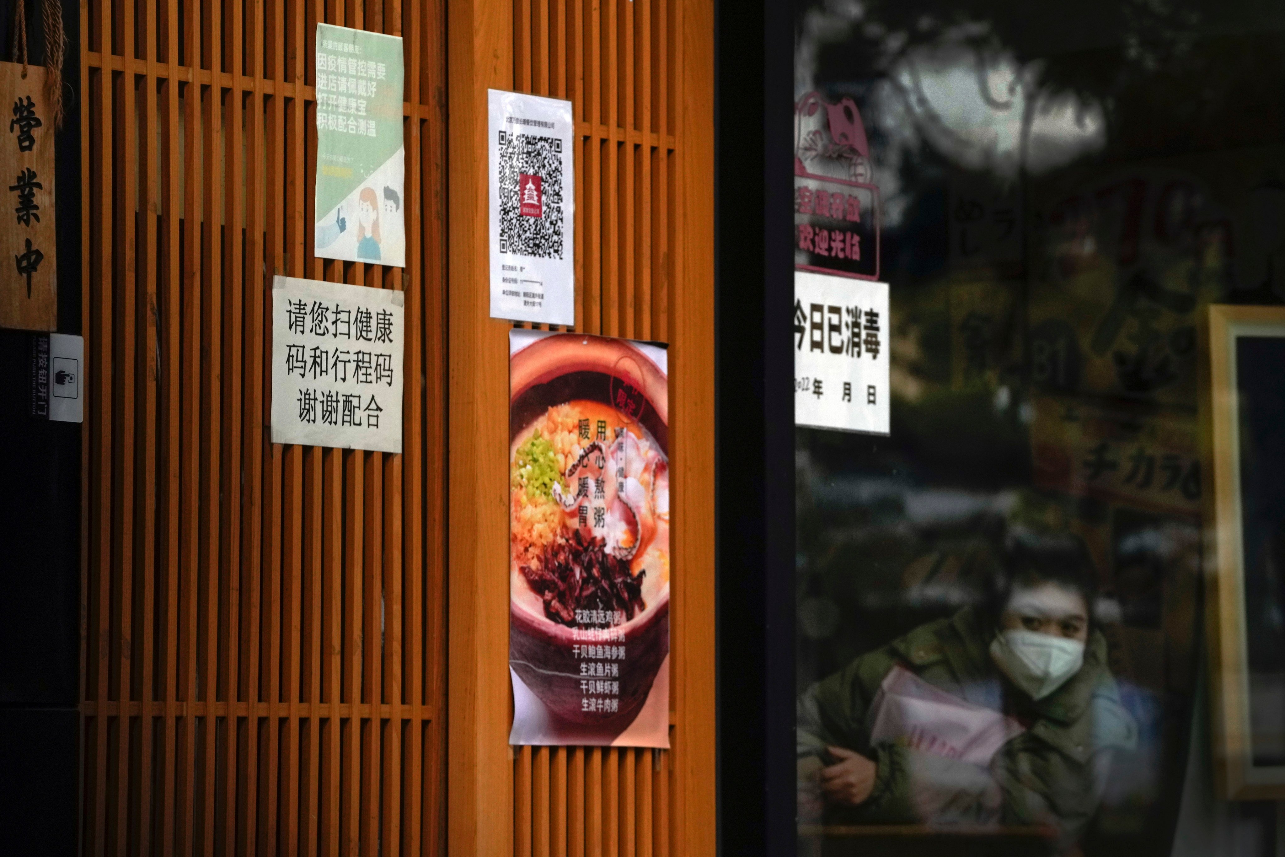 A masked worker looks out from a restaurant as its entrance door displays a health check QR code on December 12. China will drop a travel tracing requirement as part of an uncertain exit from its strict “zero-Covid” policies that have elicited widespread dissatisfaction. Photo: AP
