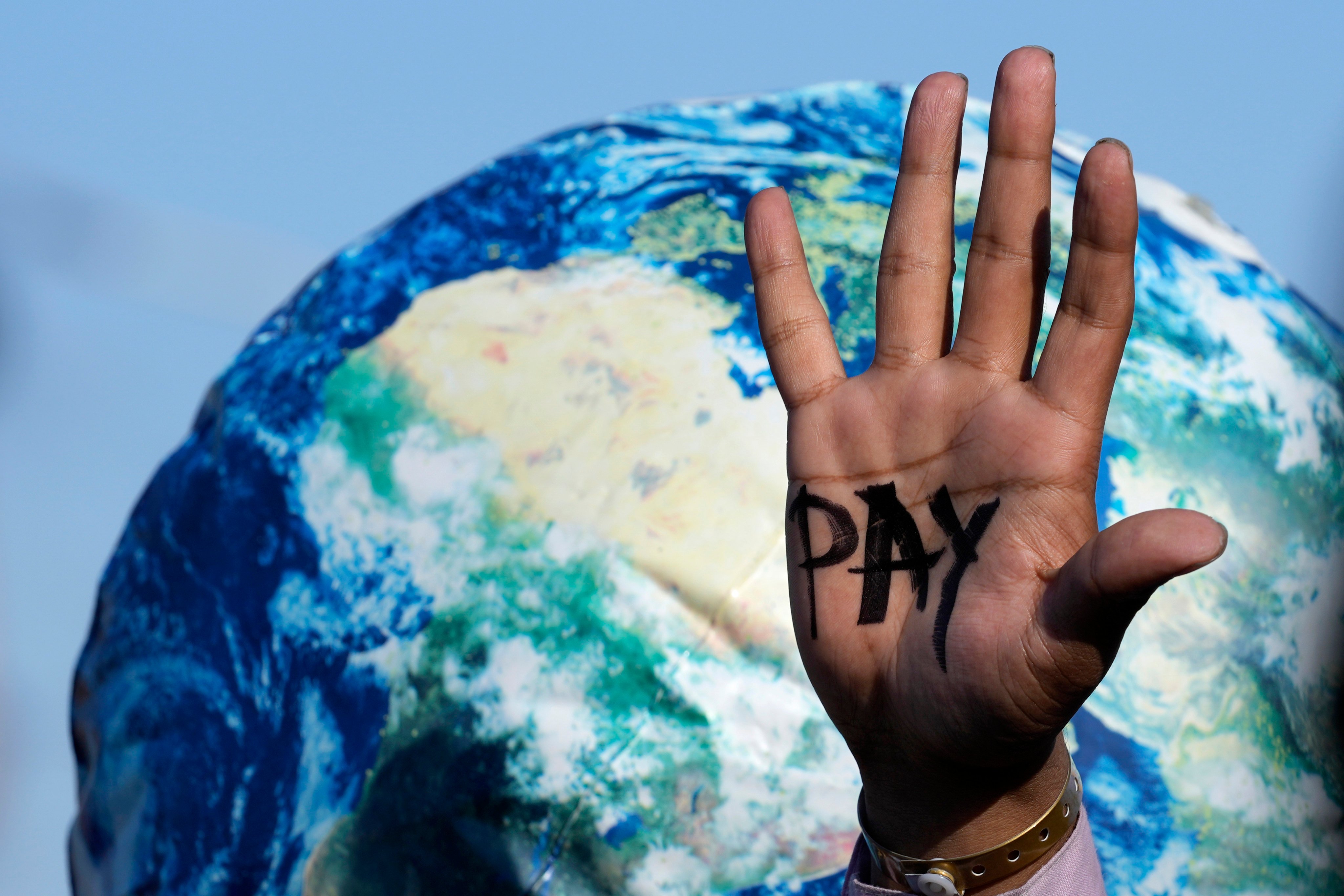 A hand reads ‘pay’ calling for reparations for loss and damage at the COP27 UN Climate Summit, in Sharm el-Sheikh, Egypt, on November 8, 2022. Photo: AP Photo