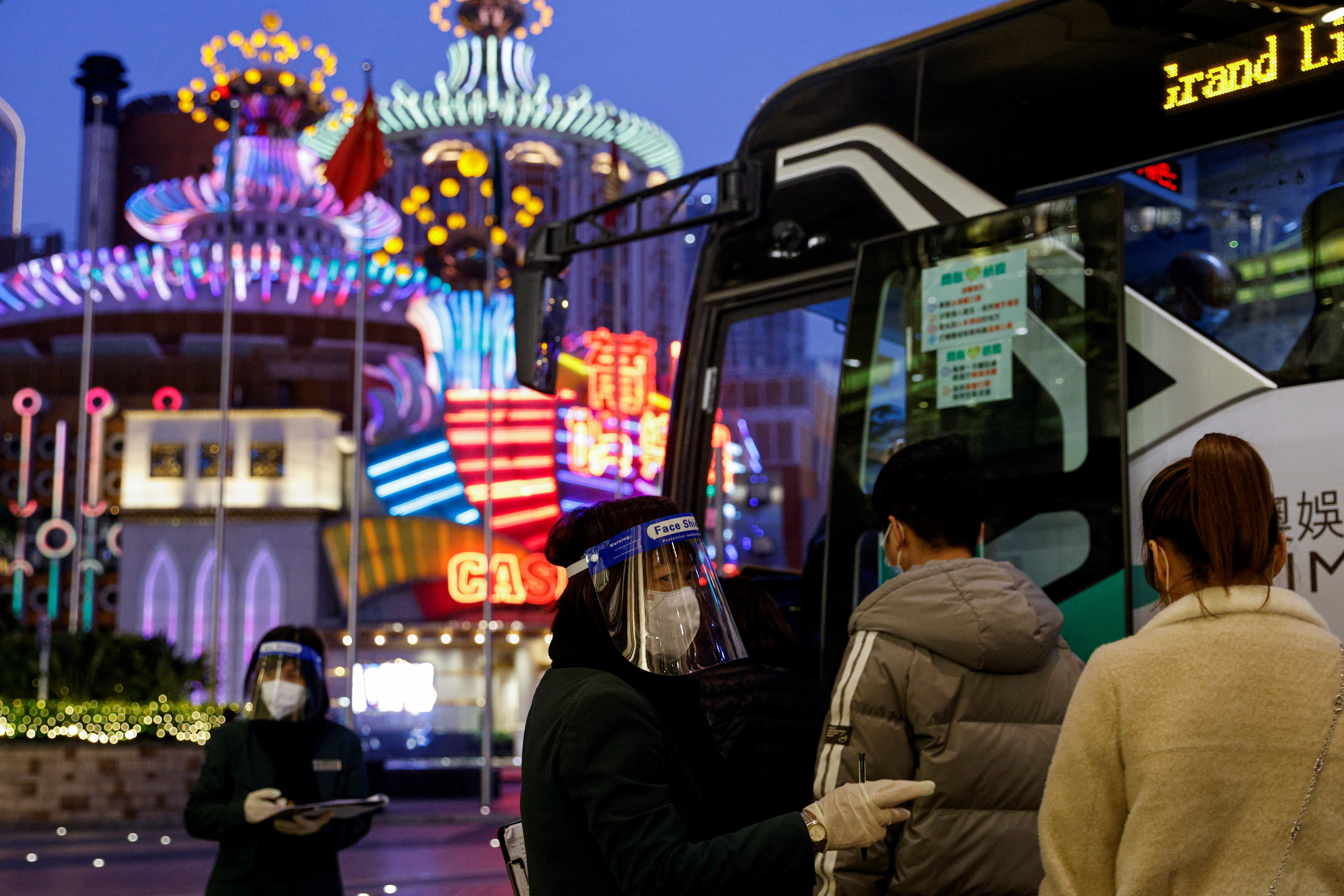 An employee wearing a mask and a face shield engages with people boarding a shuttle bus for casinos in Macau on December 29, 2022. Photo: Reuters 