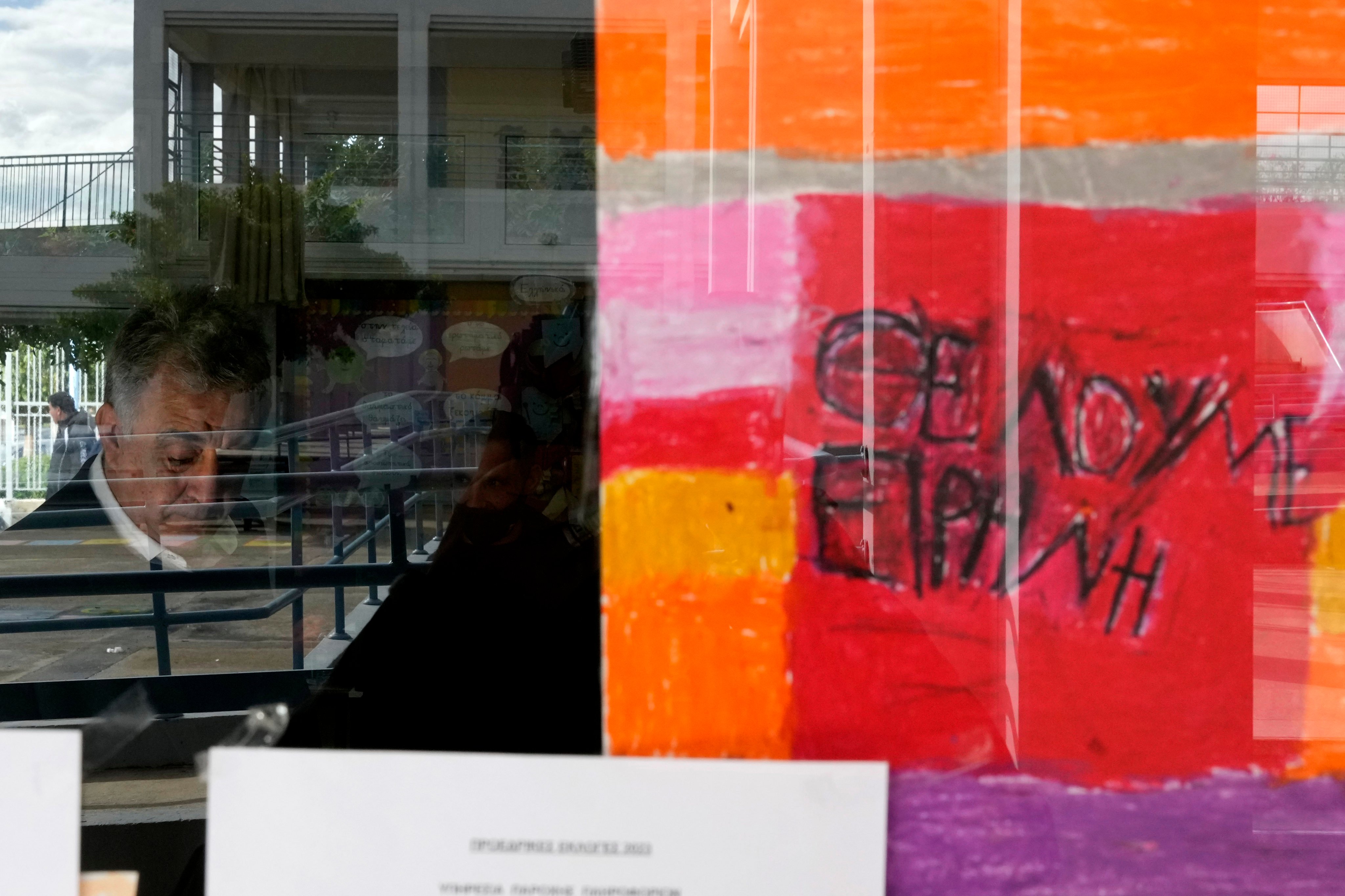 A painting on a classroom window reads “We need Peace” in Greek as a man casts his vote during the Cypriot presidential elections. Photo: AP