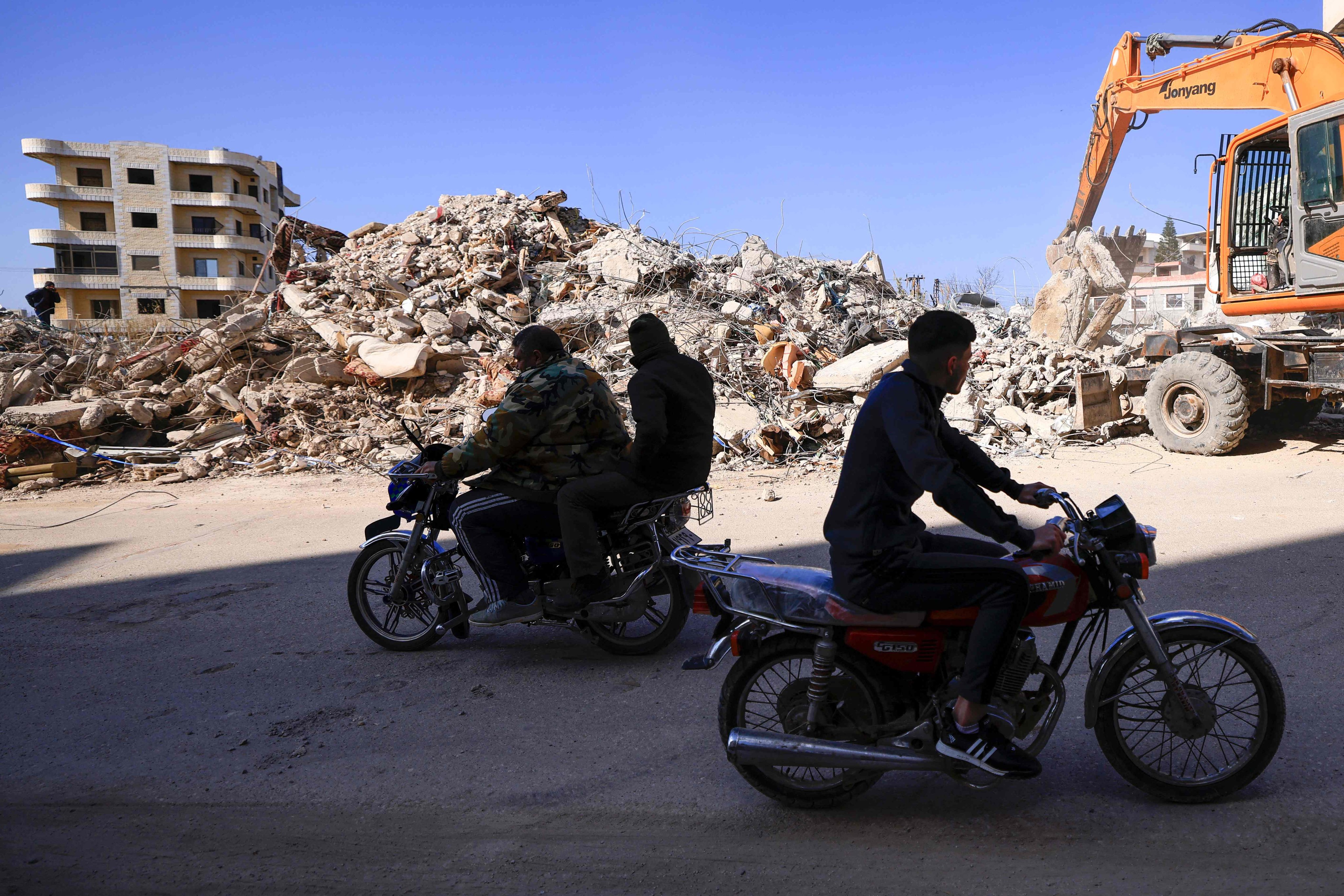 People ride their motorcycles past a destroyed building as search and rescue operations continue in the regime-controlled town of Jableh in the province of Latakia, northwest of the Syrian capital, on February 12. Photo: AFP