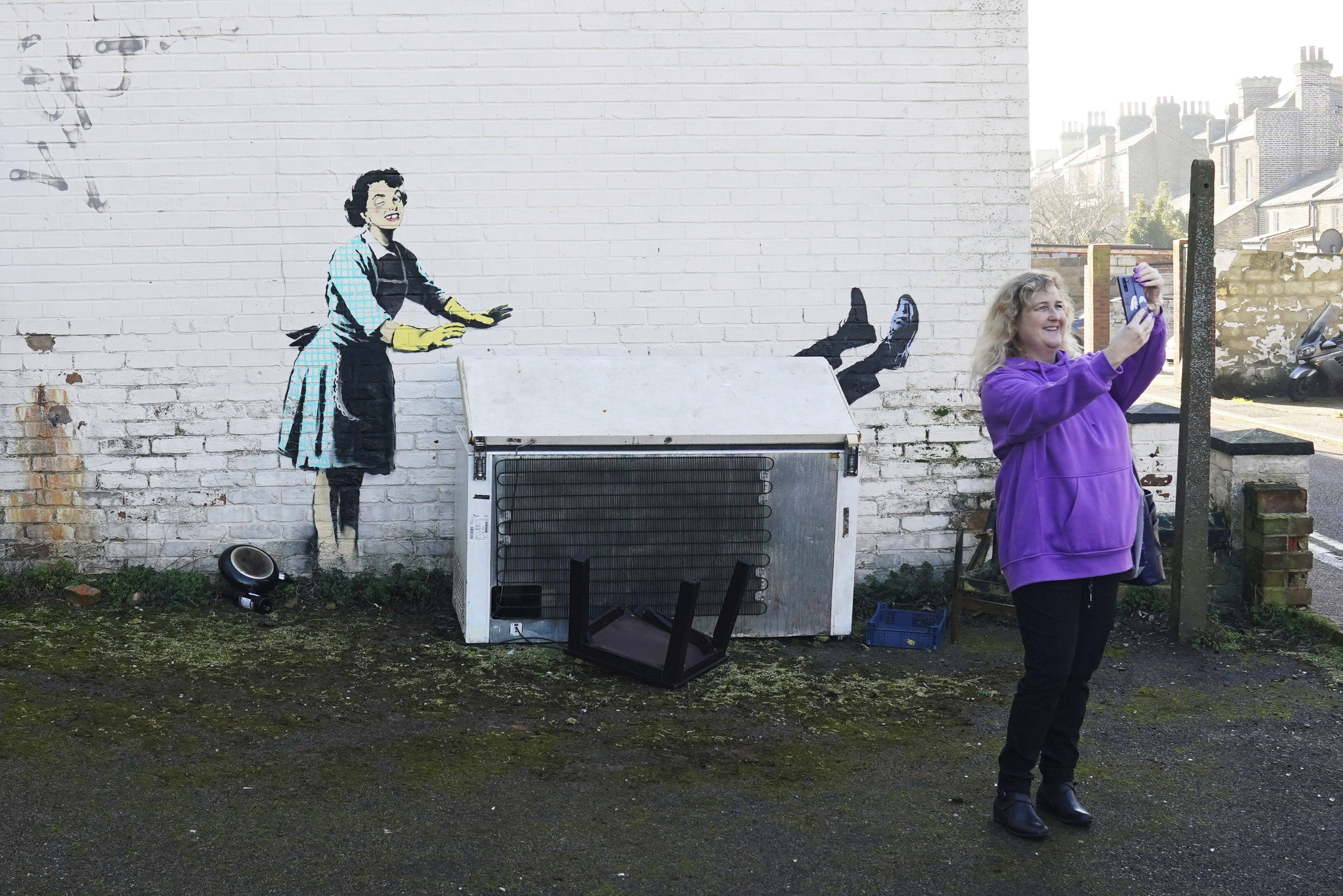 A woman takes a picture with a new artwork by street artist Banksy, titled “Valentine’s Day Mascara” in Margate, England on Tuesday. Photo: PA via AP