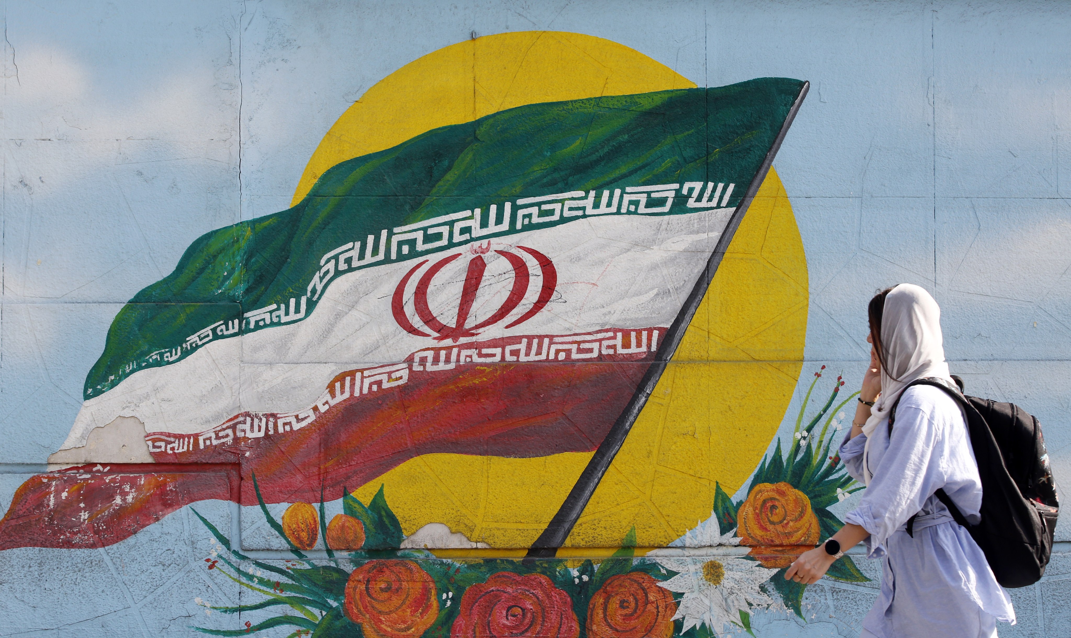 A woman wearing a headscarf walks past graffiti showing the Iranian national flag in Tehran, Iran. Photo: EPA-EFE