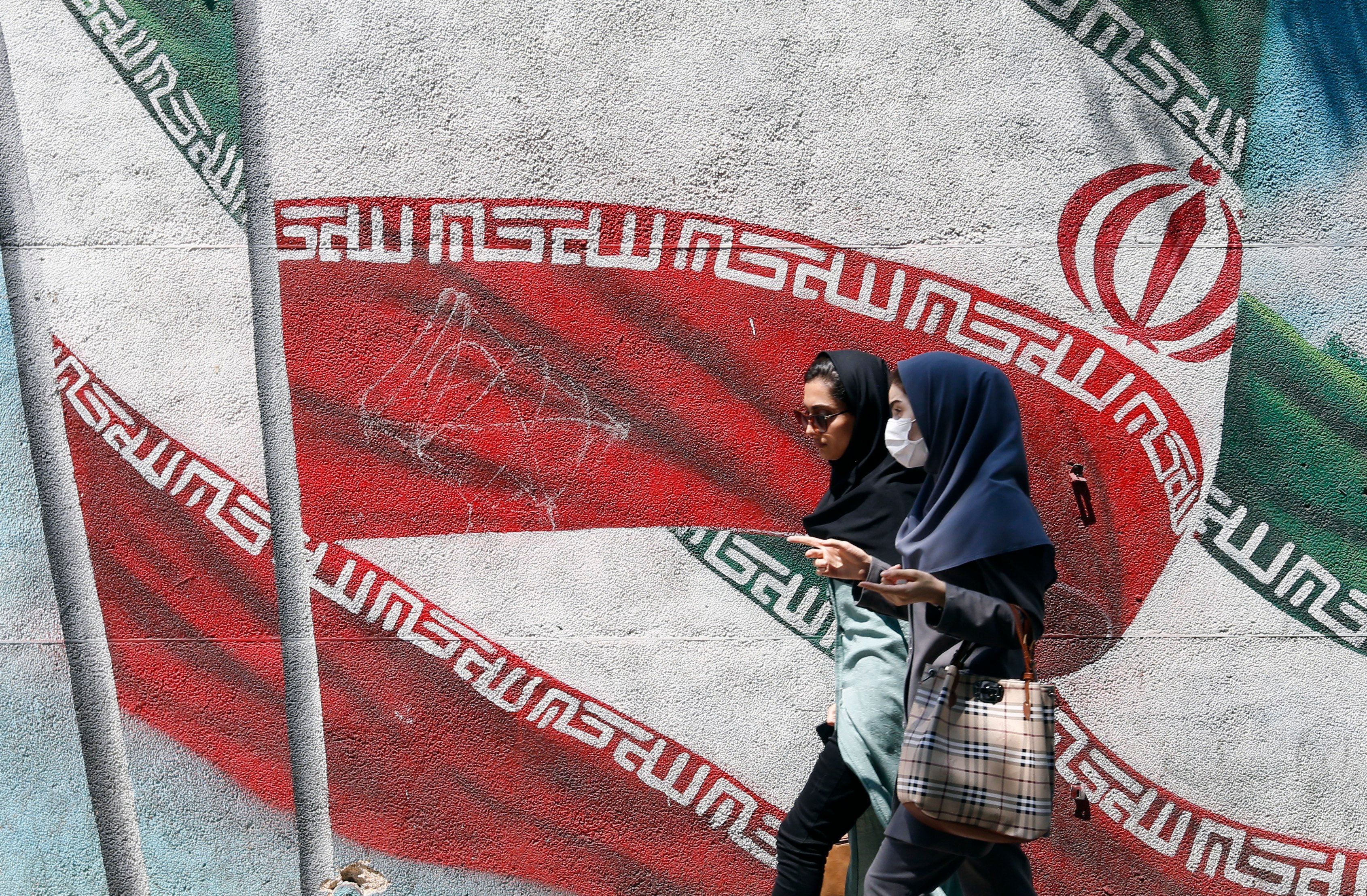 Young Iranians walk past a painting of Iran’s national flag in a street in Tehran. There are reports some schoolgirls are being poisoned to prevent them learning. File photo: EPA-EFE