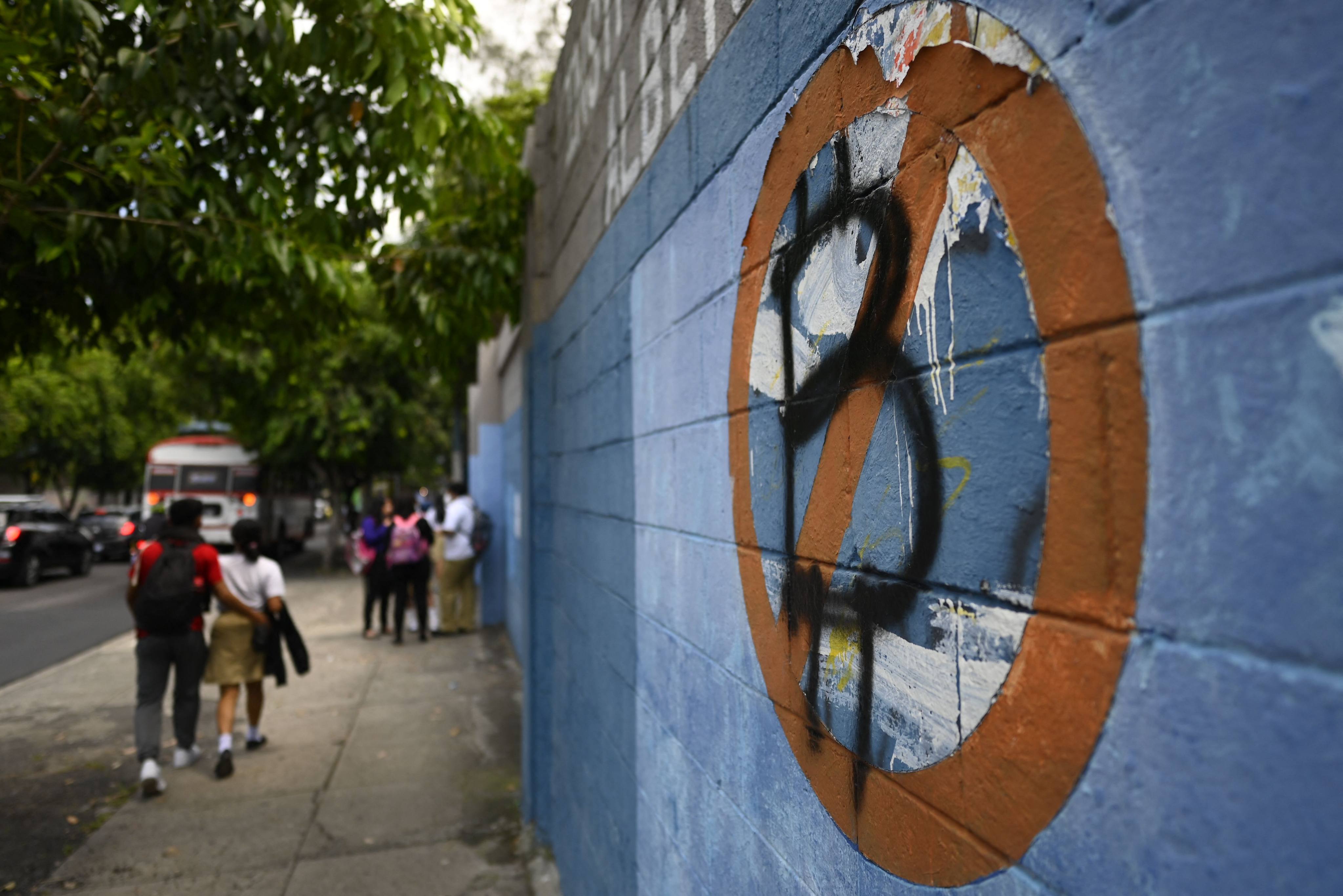 Students walk past a wall painted with an anti-bitcoin protest symbol in San Salvador, El Salvador, on October 18, 2022. The boom and bust in cryptocurrency markets in the past three years has sparked fears among regulators and efforts to rein in digital currencies and their associated technology. Photo: AFP