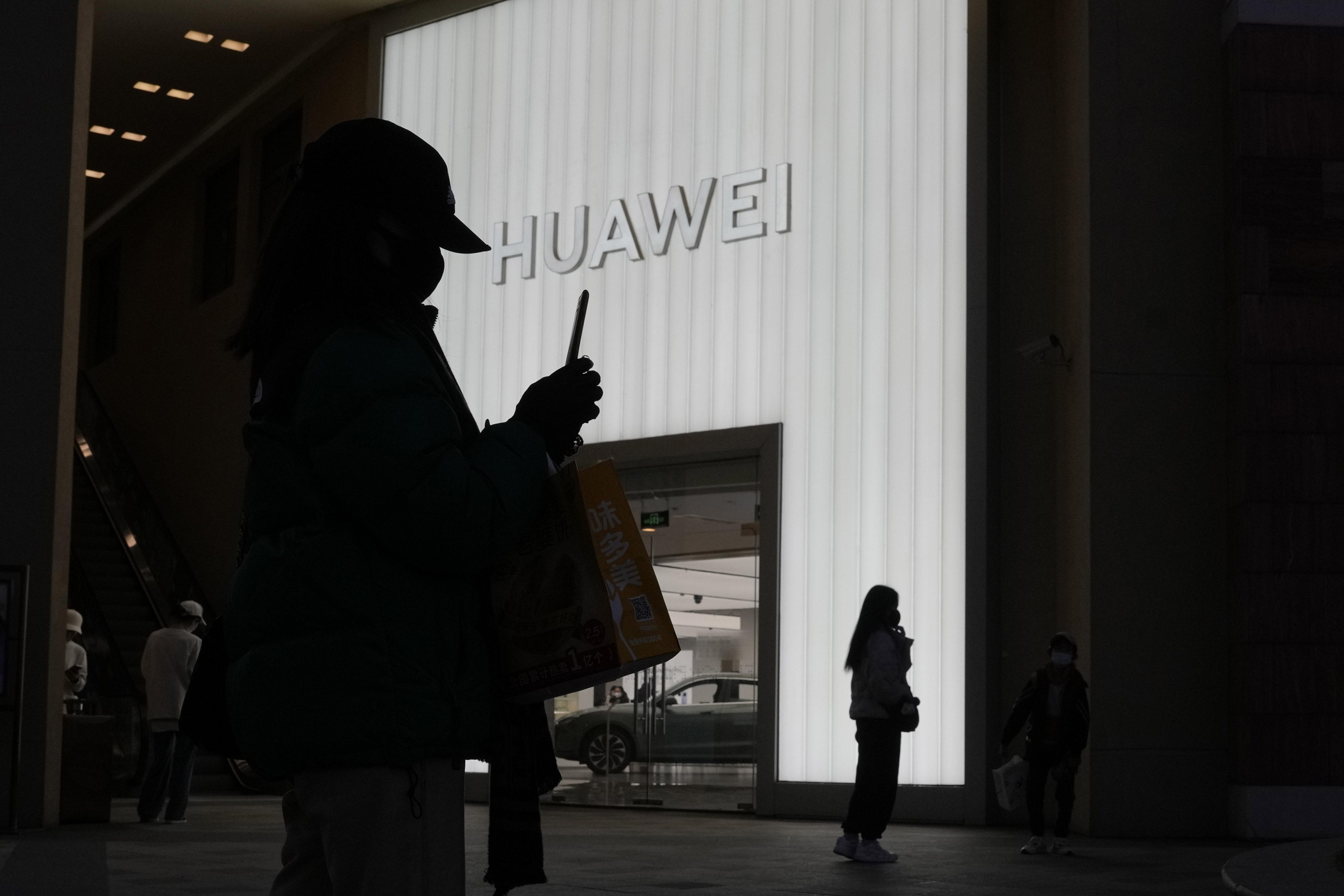 Shoppers are silhouetted outside a retail store of Huawei Technologies Co in Beijing on December 30, 2022. Photo: AP