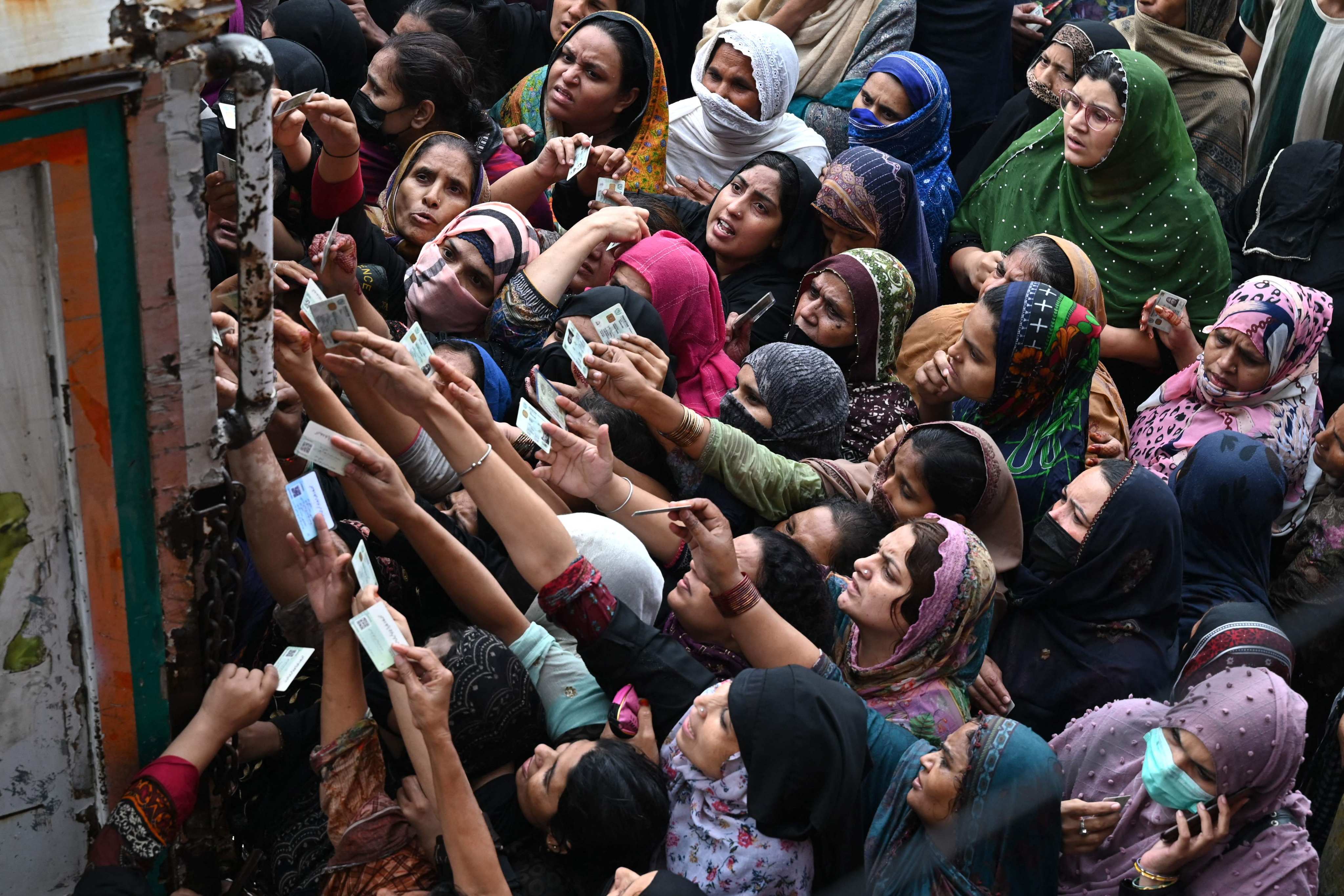 Women show their national identity cards to receive free bags of flour from a delivery truck in Lahore last week before the start of Ramadan. Photo: AFP