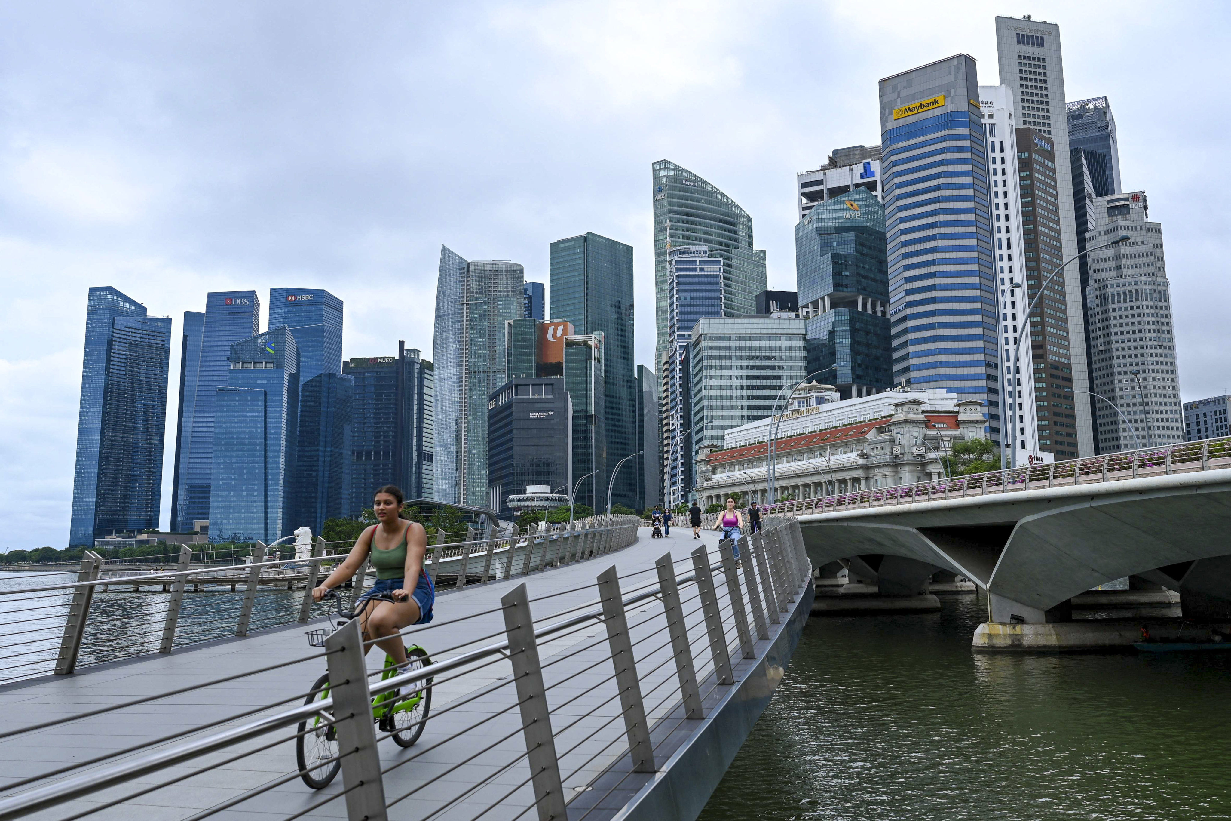 People ride bikes across a bridge next to Singapore’s business district on April 7. While the dramatic rise in rents has caused some mid-level management staff to have second thoughts about staying in Singapore, the city-state continues to attract capital and expertise from the West, China and the rest of Asia. Photo: AFP