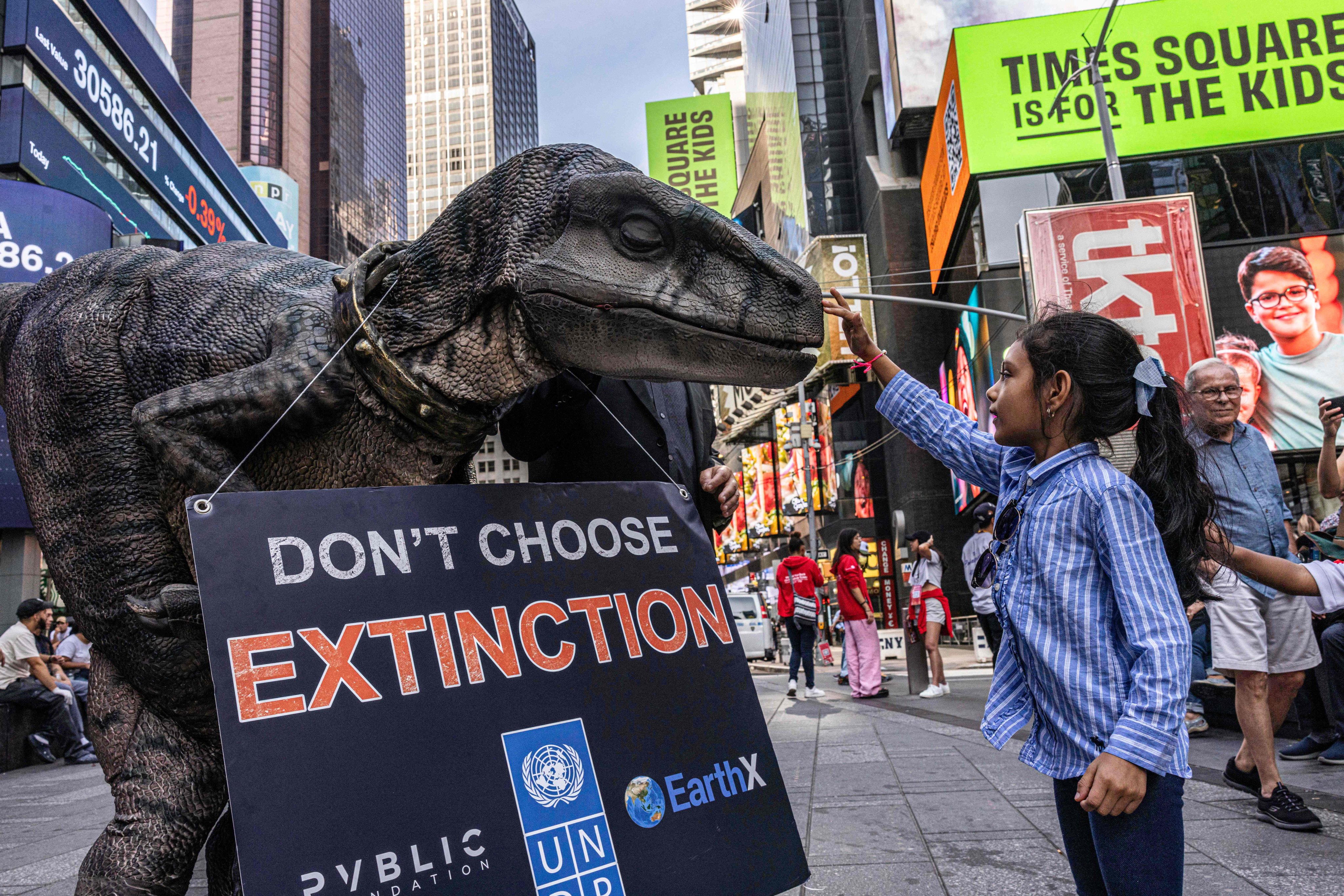 A young girl pets Frankie the Dinosaur, mascot of the UNDP’s “Don’t Choose Extinction” campaign, in Times Square, New York on September 21, 2022. Photo: AFP