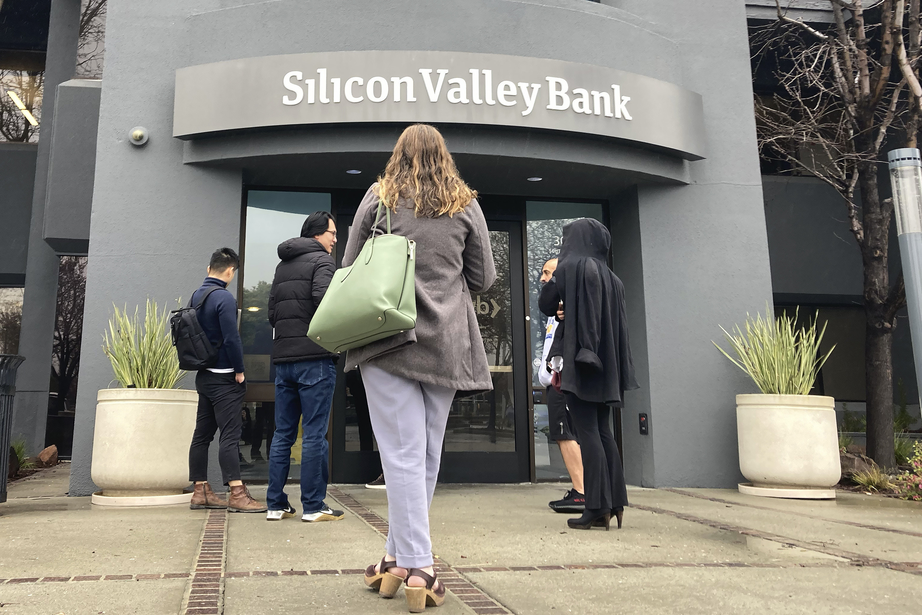 People stand outside an entrance to Silicon Valley Bank in Santa Clara, California, on March 10. The sustained rise in interest rates has helped drive the turmoil currently shaking markets, but a sudden shift to central banks cutting rates appears unlikely. Photo: AP