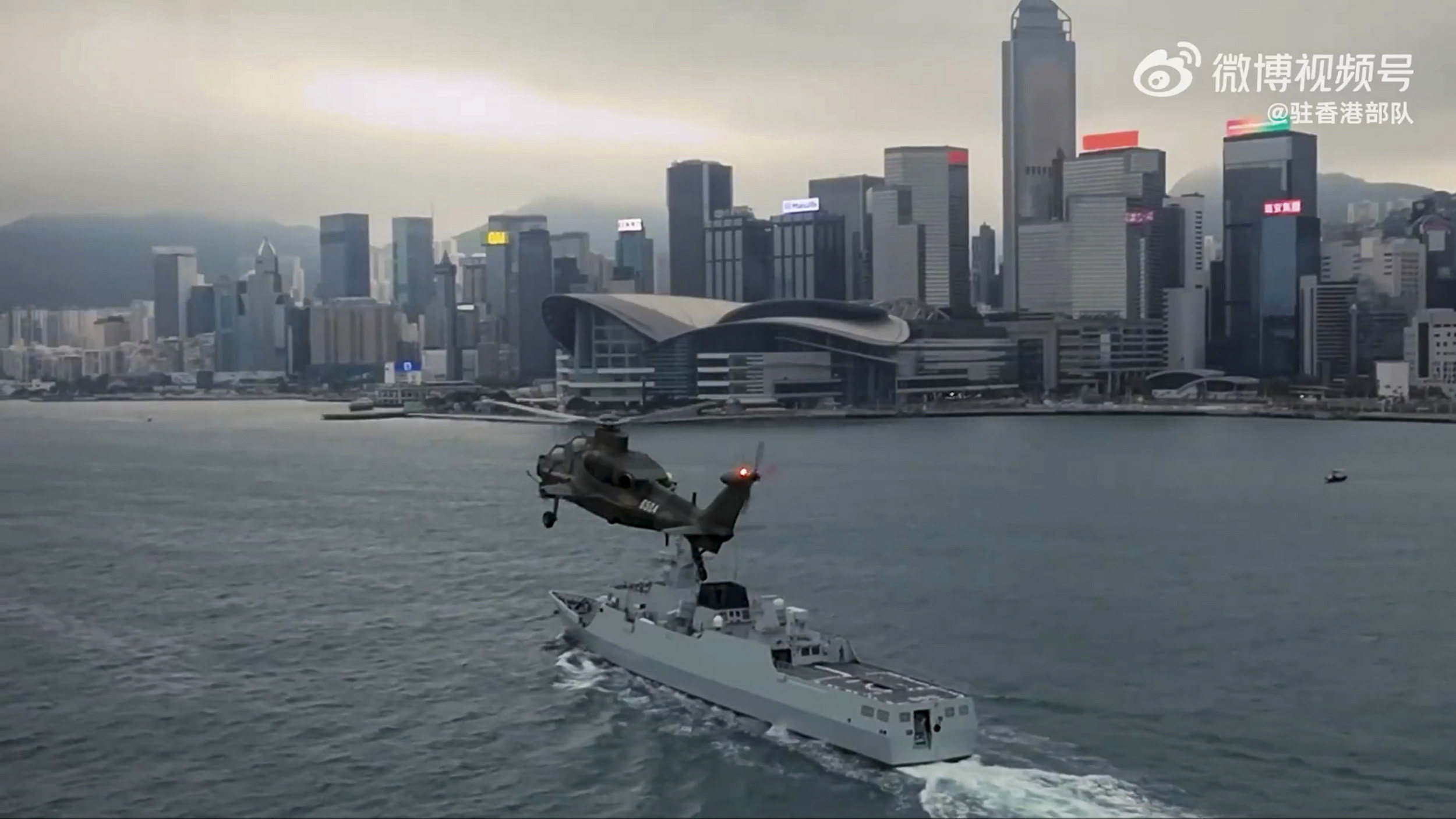 A helicopter and warship pass in front of the Hong Kong Exhibition and Convention Centre. Photo: Weibo