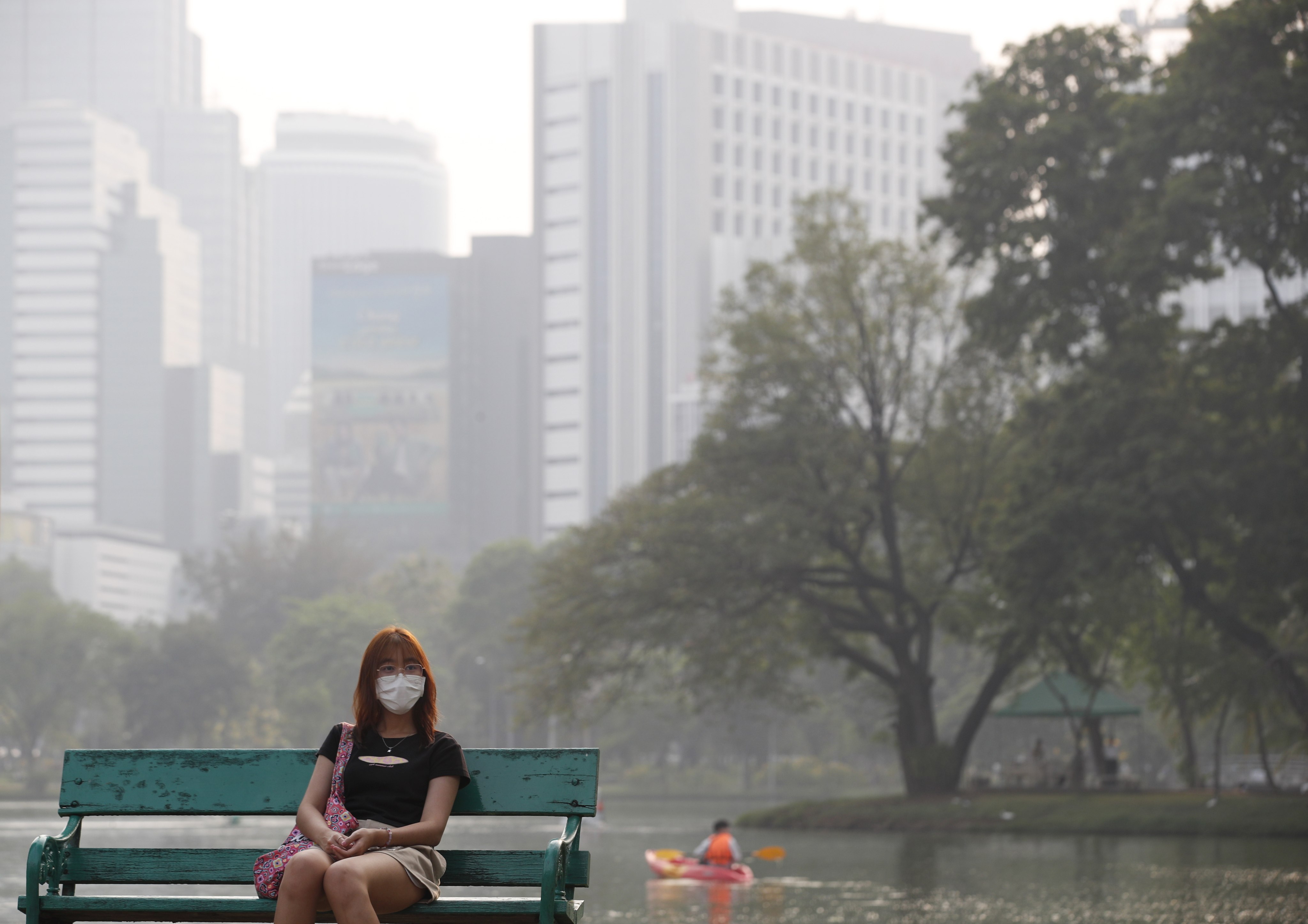 A woman sits on a bench in Bangkok’s  Lumpini Park as smog shrouns the Thai capital on 10 March 2023. Photo: EPA-EFE