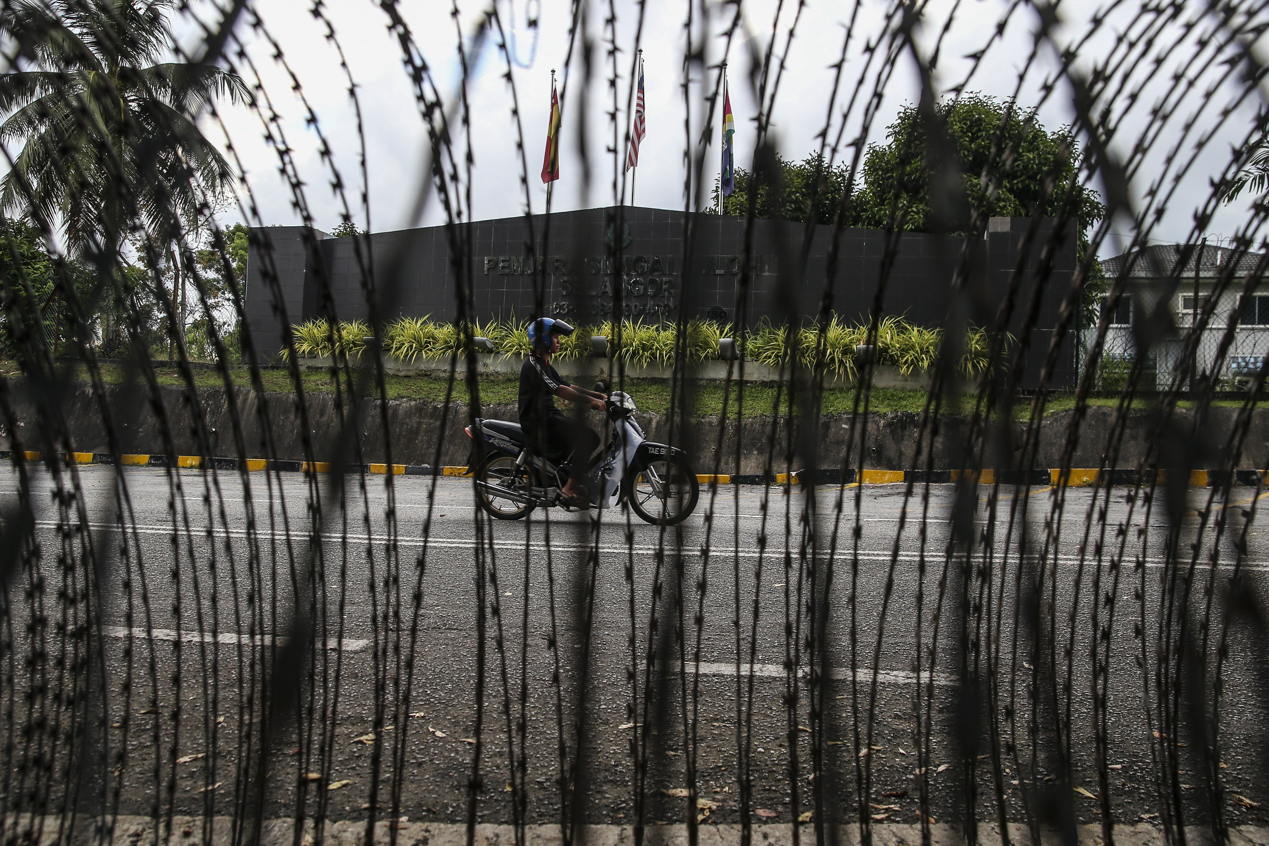 A motorcyclist is seen between barbed wire fence at the entrance of Sungai Buloh Prison in Malaysia. Photo: EPA-EFE