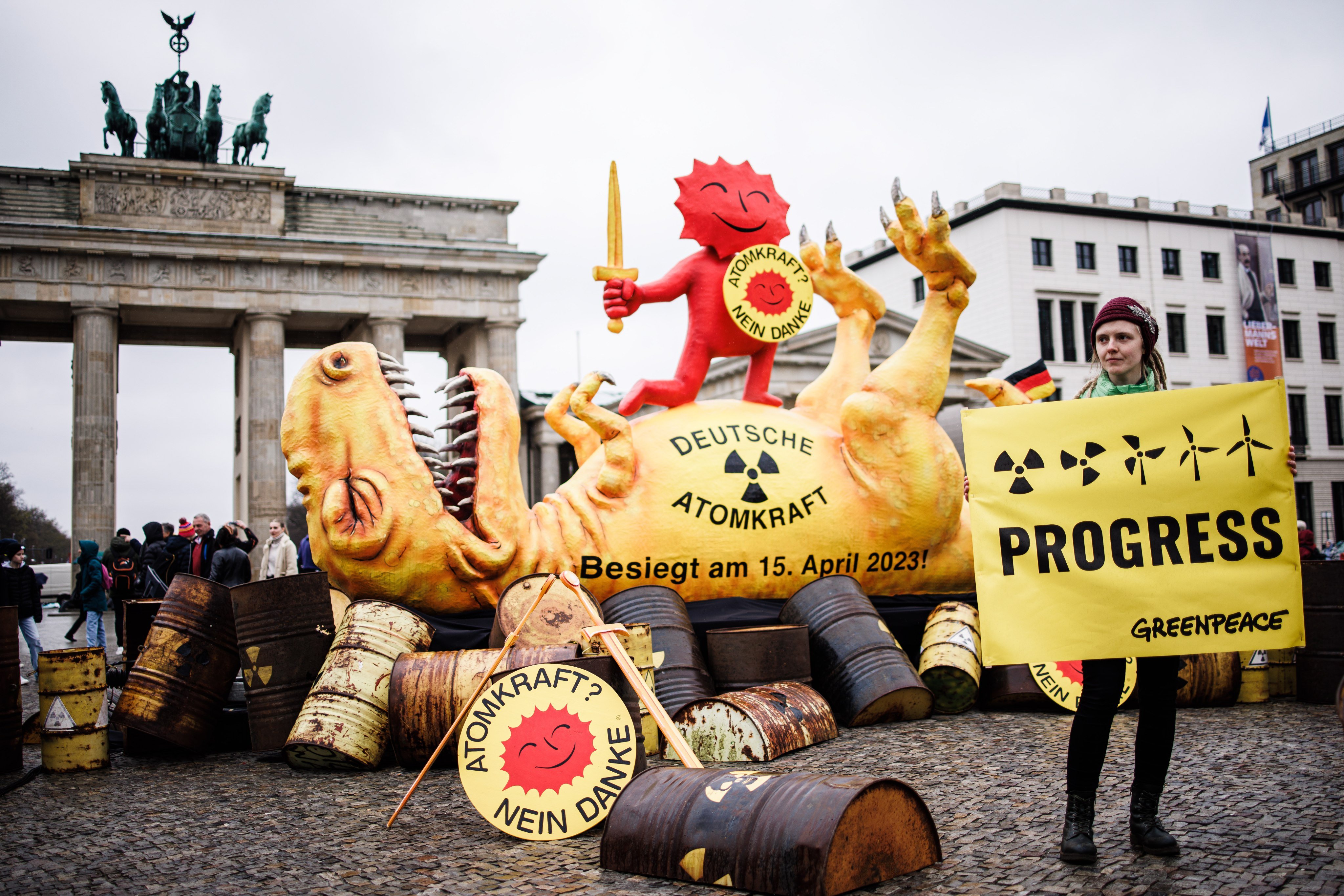An activist poses with a placard in front of a sculpture of a dead dinosaur during a protest of the environmental organization Greenpeace in front of the Brandenburg Gate in Berlin on April 15, 2023. Photo: EPA-EFE
