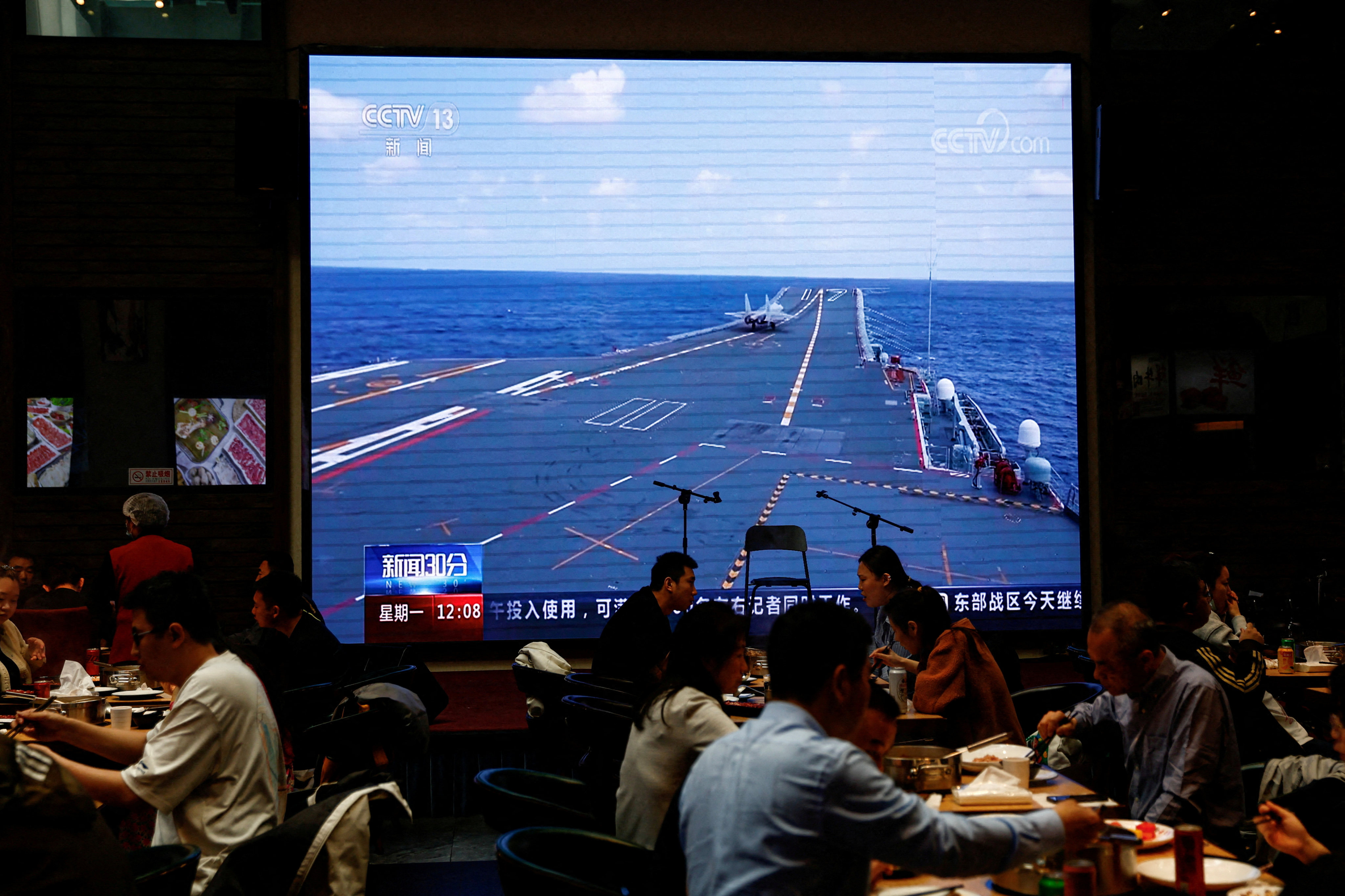 Customers in a Beijing restaurant dine as a giant screen broadcasts news footage of an aircraft taking off from the Shandong aircraft carrier as part of “Joint Sword” exercises around Taiwan by the People’s Liberation Army, on April 10. Photo: Reuters