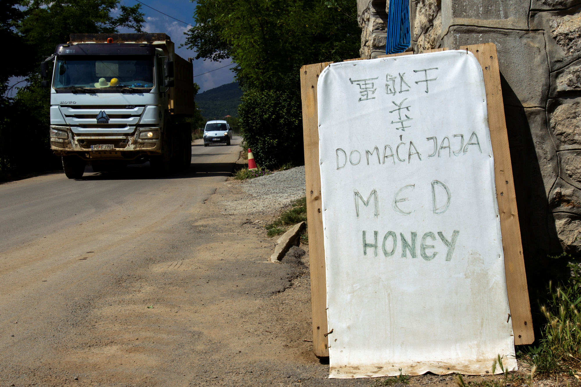 Construction trucks pass by a board advertising eggs and honey in Chinese (with the words upside down and flipped), Montenegrin and English on the Bar-Boljare highway construction site in the village of Pelev Brijeg, Montenegro on June 11, 2018. Photo: Reuters