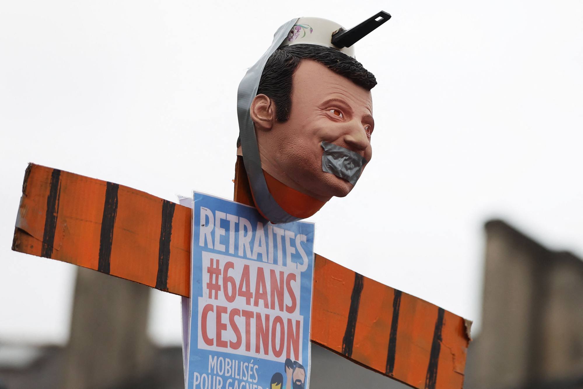 A placard reading “64 years, it’s no” with a structure representing the face of the French President Emmanuel Macron with a pan on his head during a demonstration. Photo: AFP