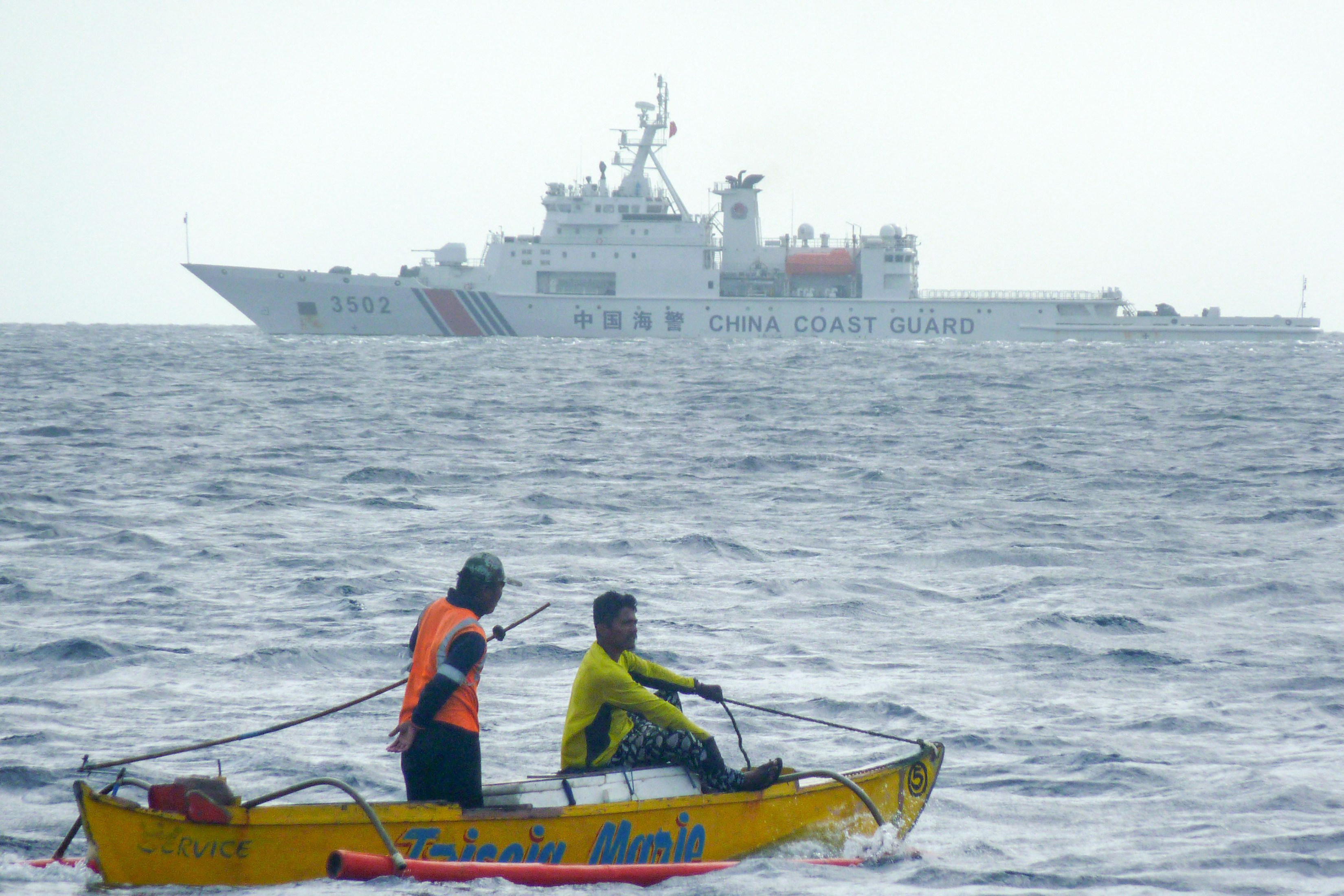 Filipino fishermen aboard a wooden boat sail past a Chinese coastguard ship in the Scarborough Shoal area of the South China Sea. Photo: AFP via Getty Images/TNS