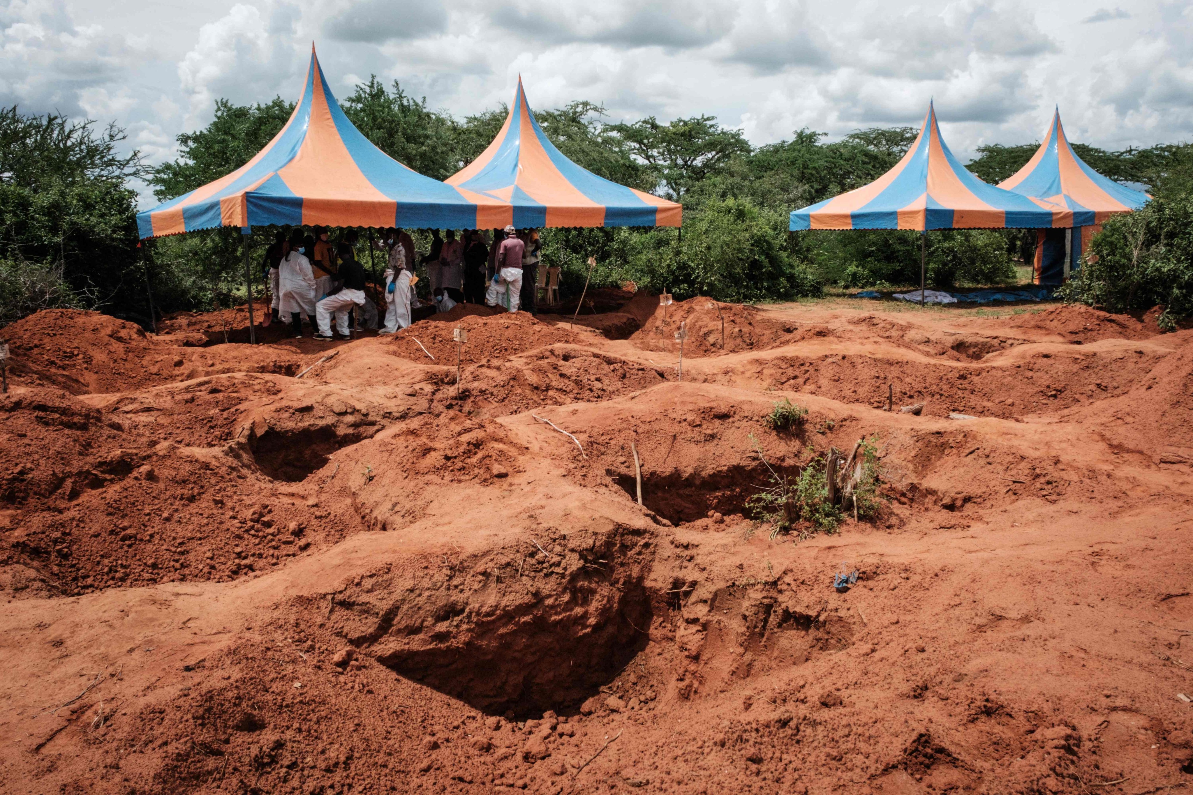 Workers take shelter while digging the ground to exume bodies from the mass-grave site in Shakahola. Photo: AFP