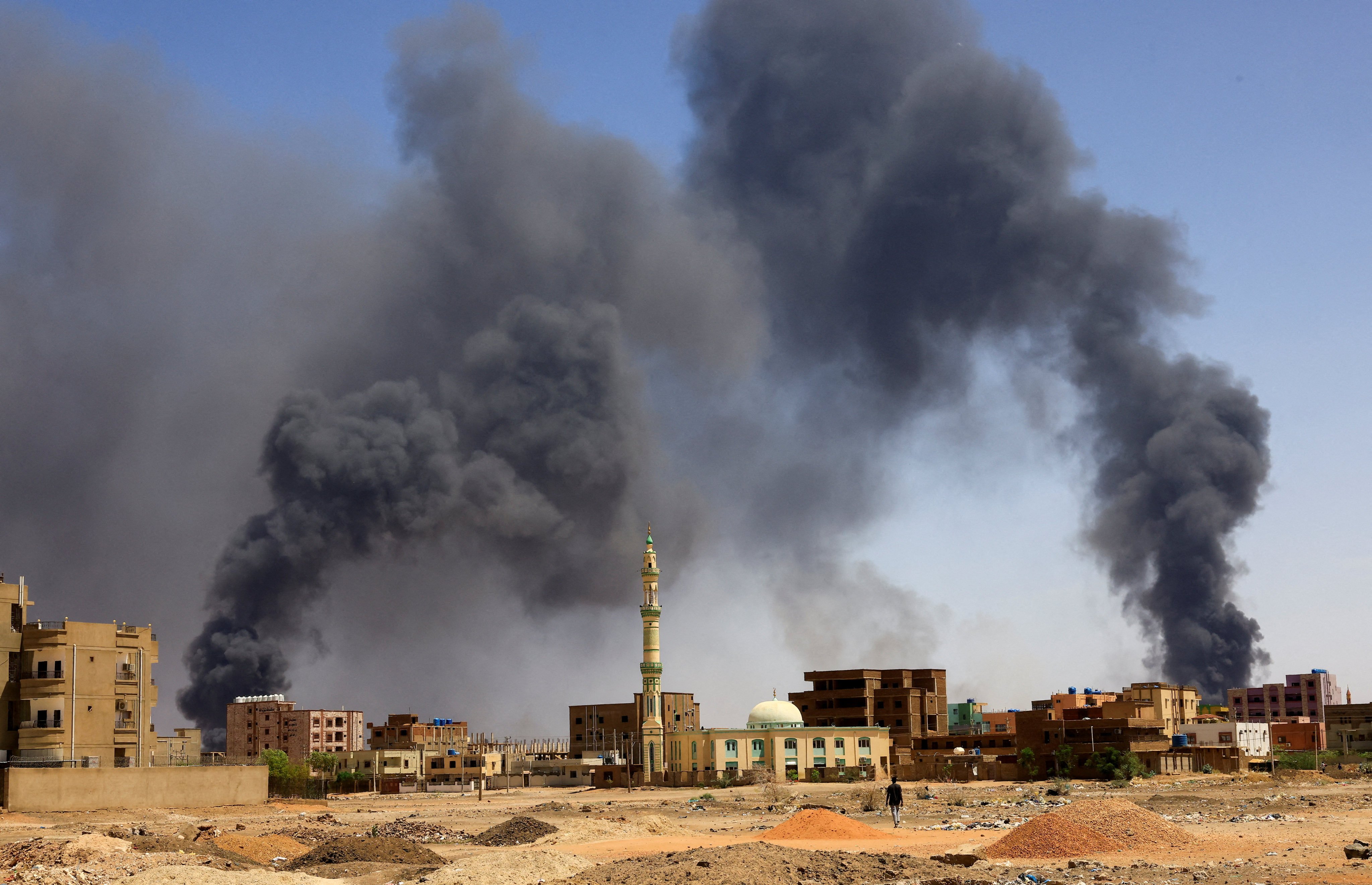A man walks while smoke rises above buildings during clashes between the paramilitary Rapid Support Forces and the army in Khartoum North, Sudan. Photo: Reuters
