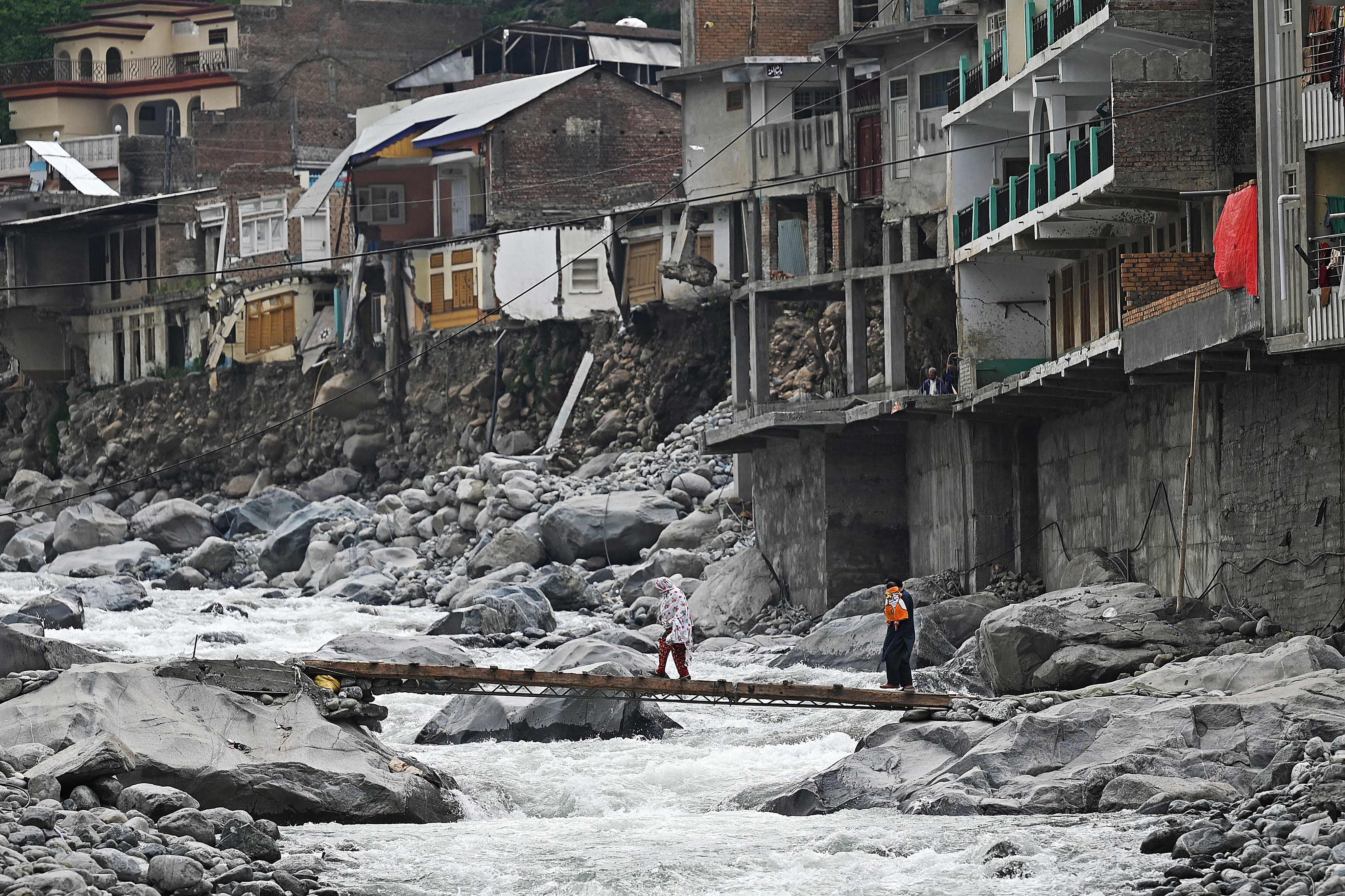 On May 4, residents cross a temporary bridge near empty hotels and houses that were damaged last year by flash floods in Bahrain, a town in Pakistan’s Swat valley. Unprecedented rains put a third of the country underwater, damaged two million homes and killed more than 1,700 people. Photo: AFP 