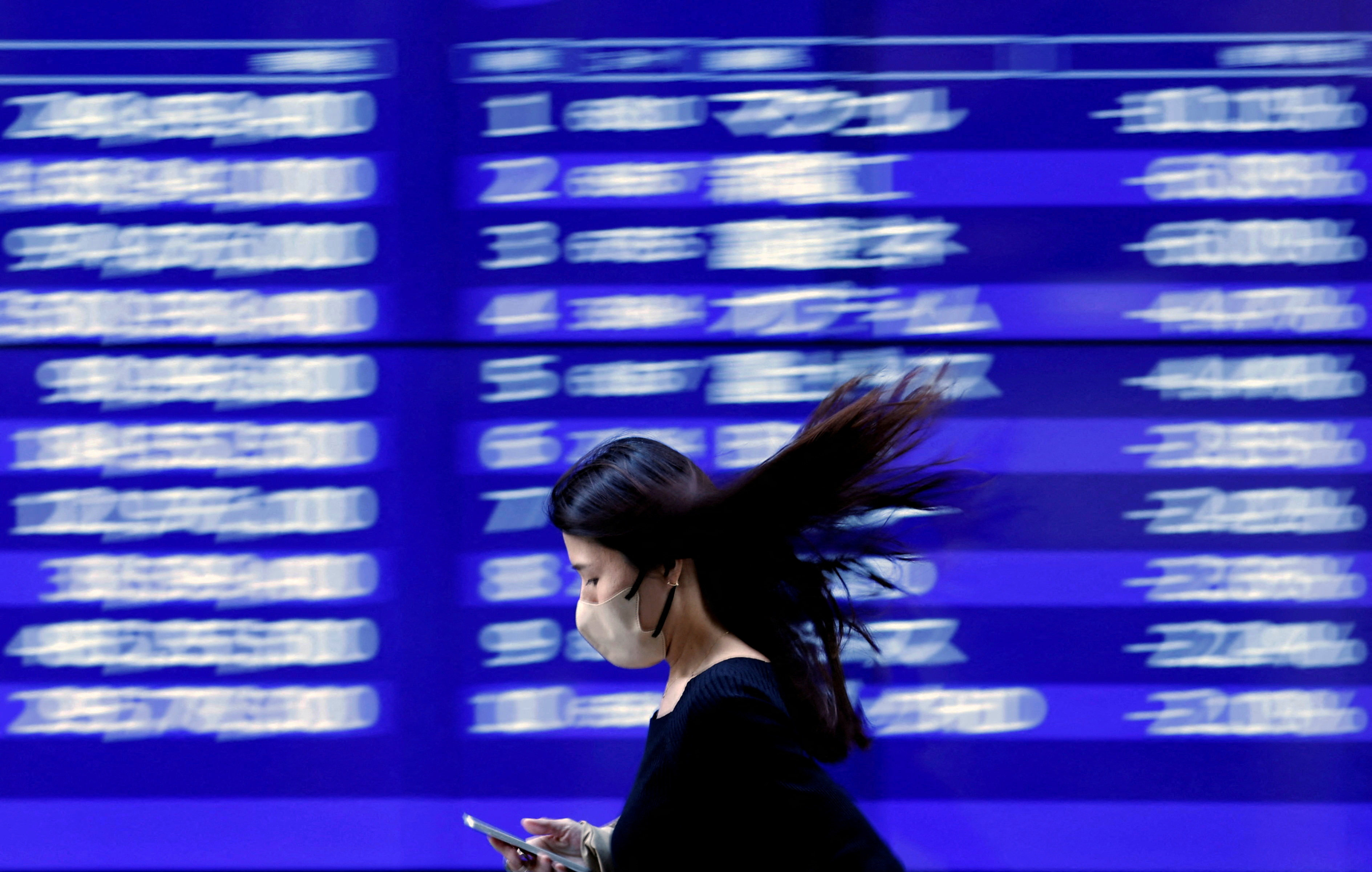 A passer-by walks past an electric monitor displaying recent movements of various stock prices outside a bank in Tokyo, Japan, on March 22, 2023. Photo: Reuters
