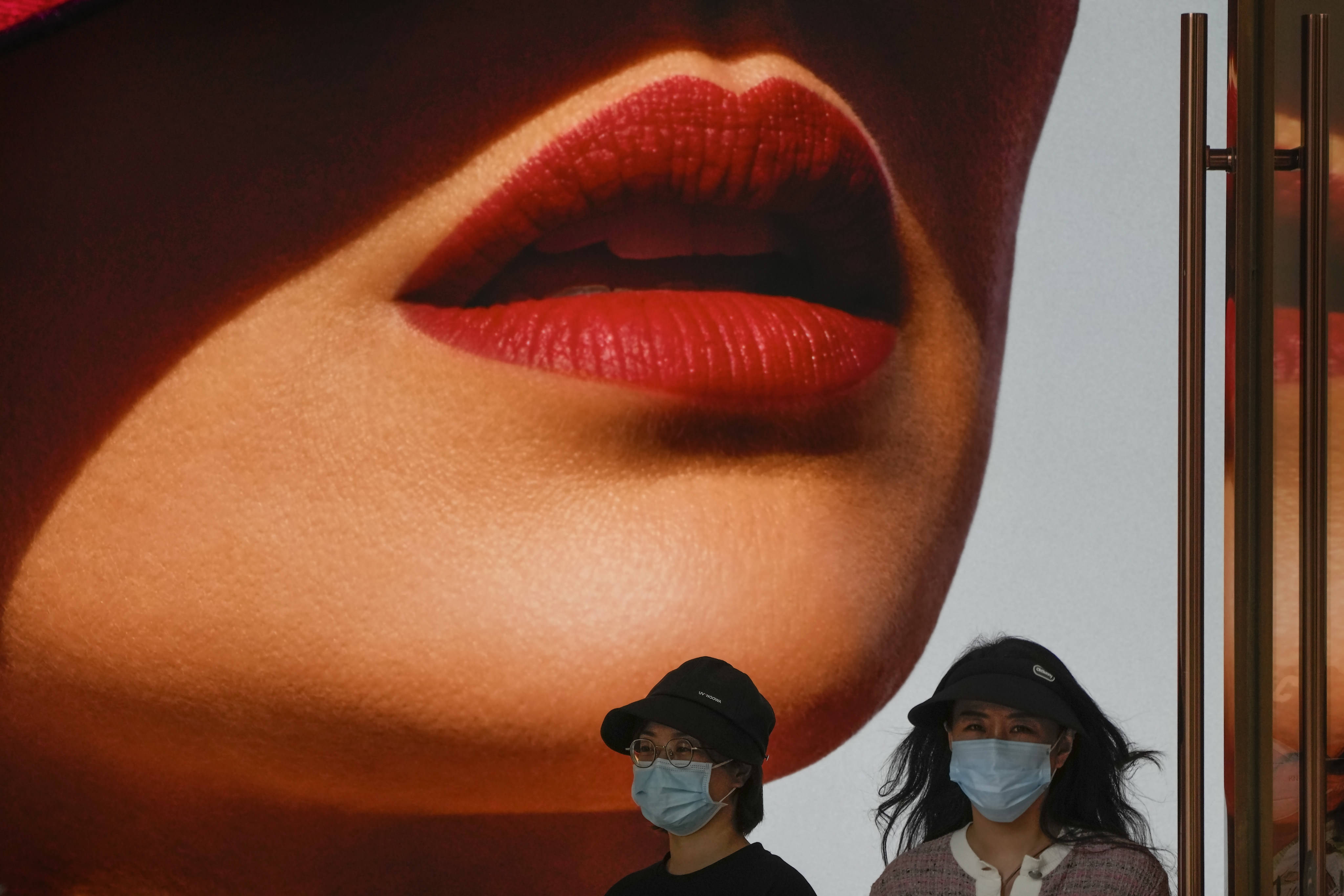 Women wearing face masks walk by a lipstick advertisement at a shopping centre in Beijing, China. Photo: AP