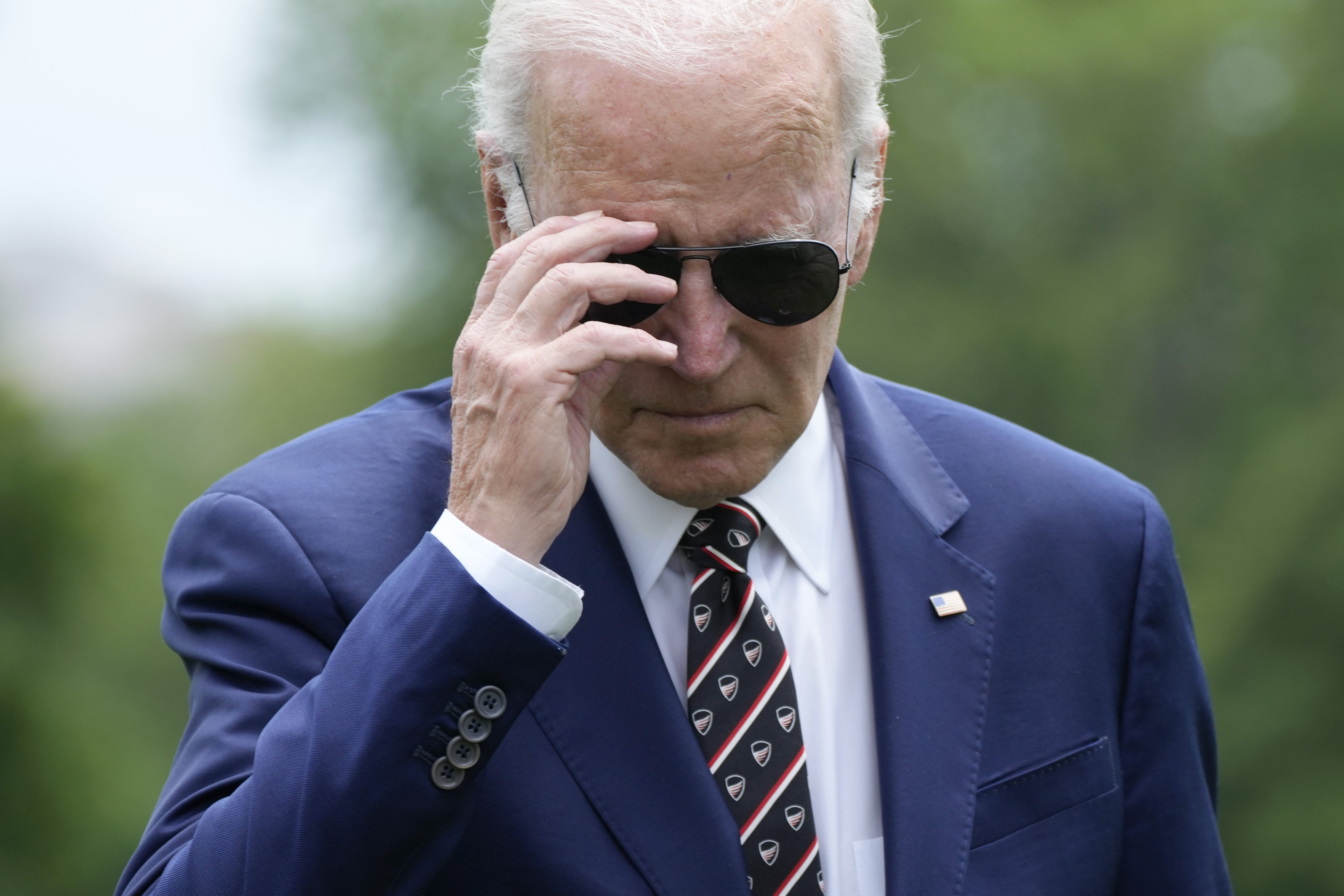 President Joe Biden removes his sunglasses as he walks to speak with reporters. Photo: AP Photo