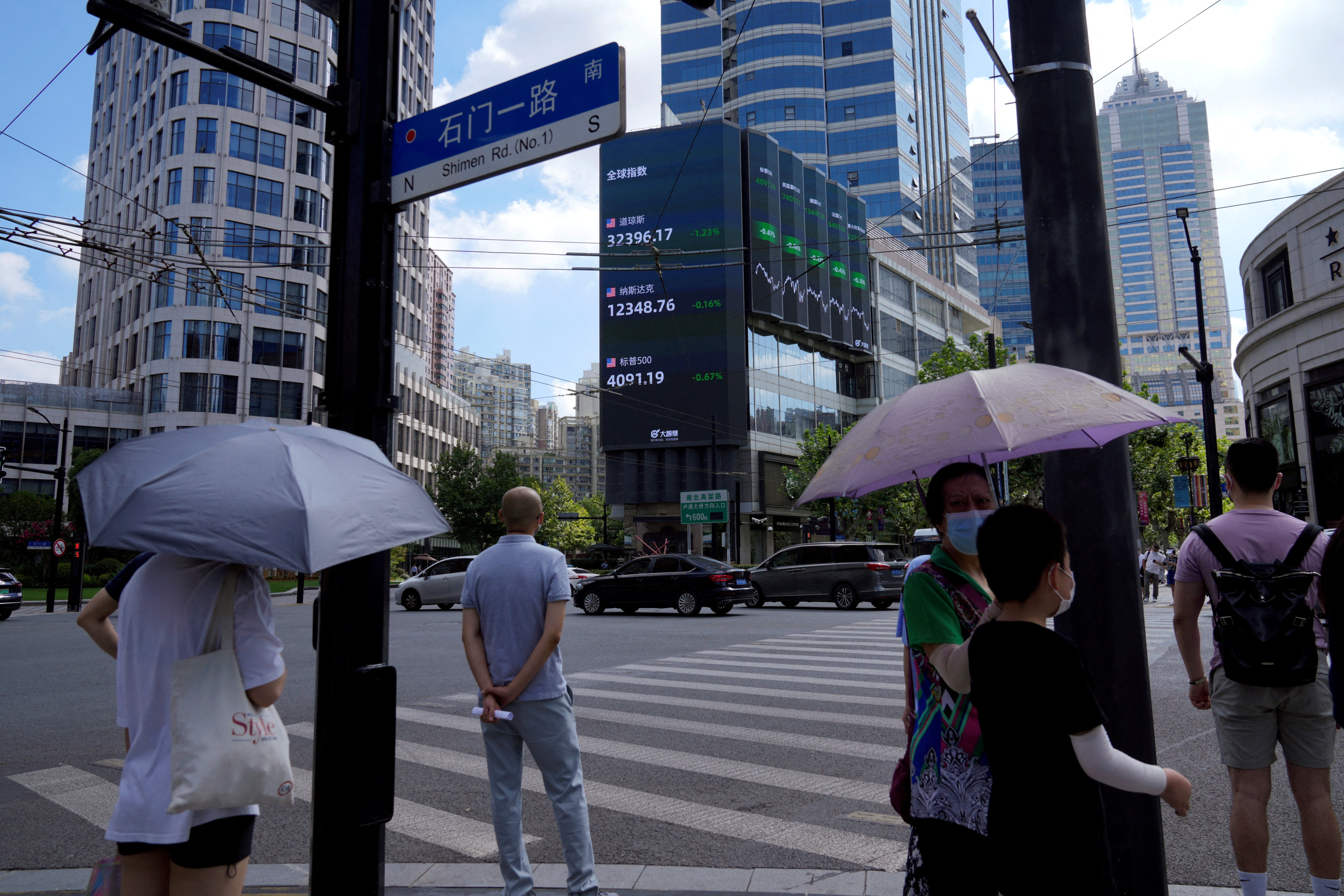 Pedestrians wait to cross a road at a junction near a giant display of stock indices in Shanghai. Photo: Reuters