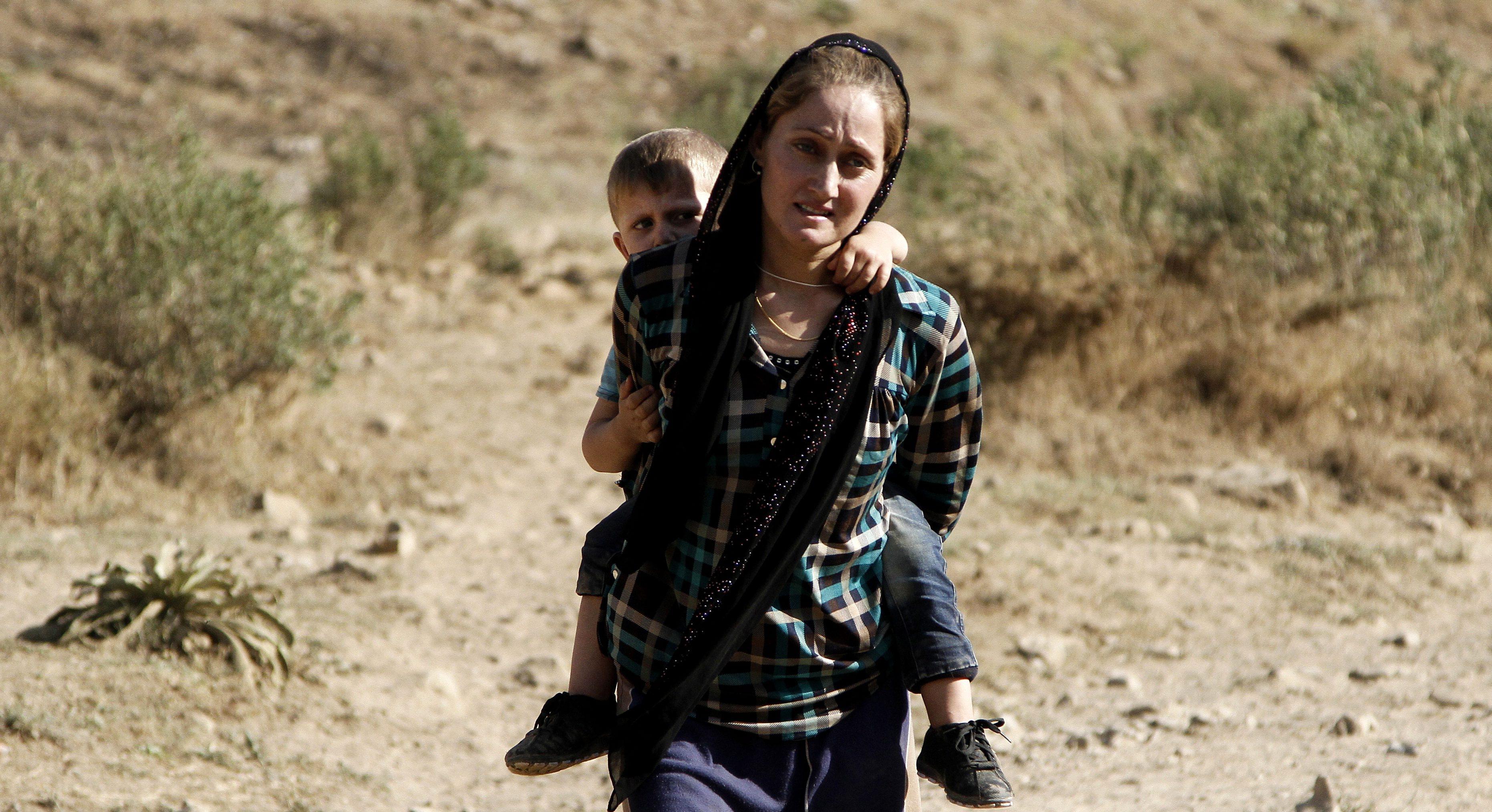 A Yazidi refugee woman carries her son on her back as they flee from Iraq in 2014. Photo: EPA