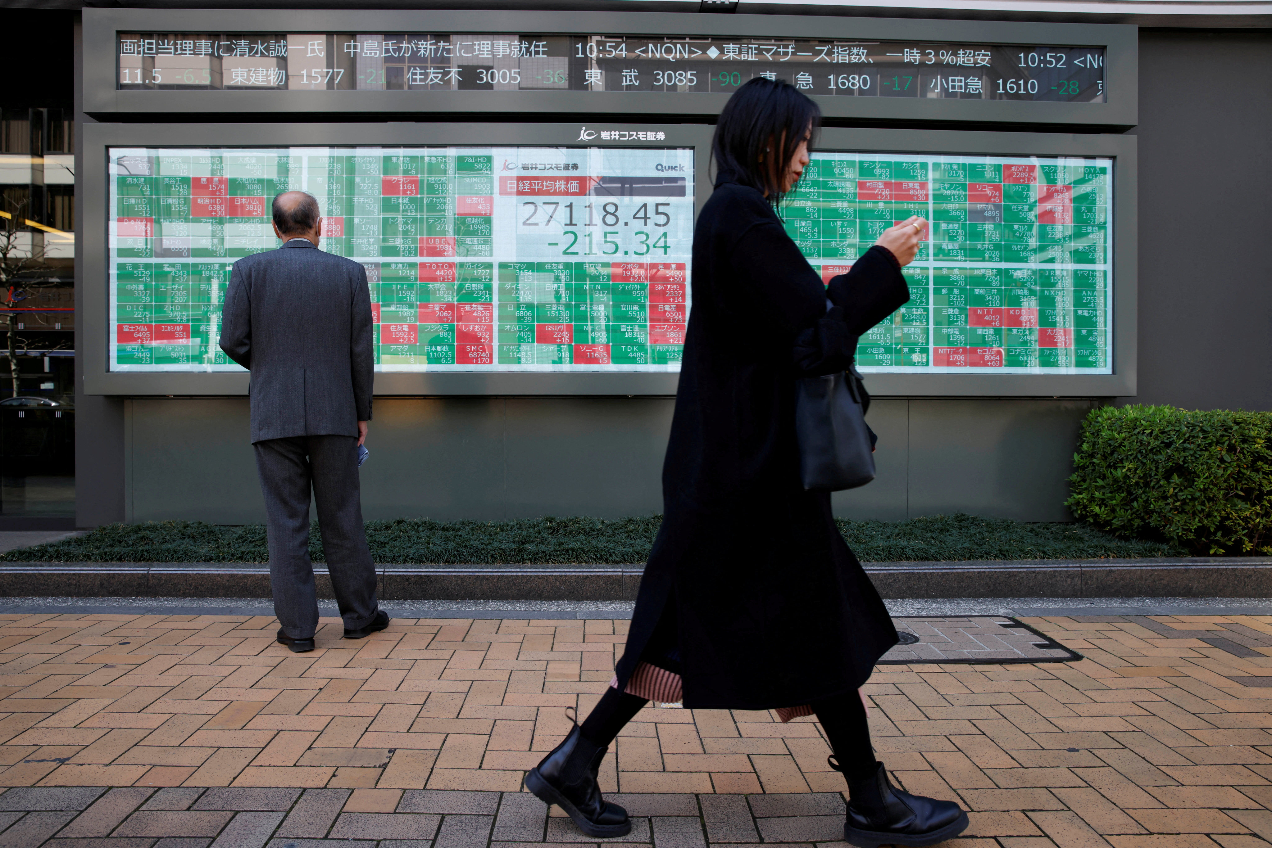 A woman walks past an electronic board showing Japan’s Nikkei average and stock prices outside a brokerage, in Tokyo in March 2023. Photo: Reuters