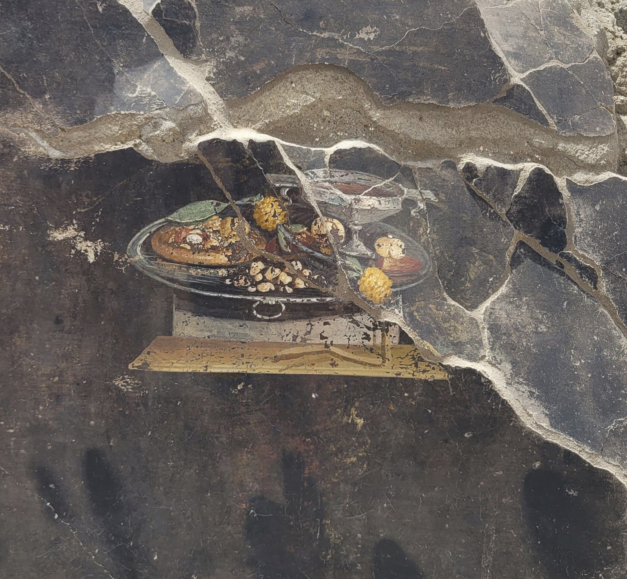 The wall of an ancient Pompeian house with a fresco depicting a table with food. The fresco was found in the atrium of a house in Insula 10 of Regio IX under excavation, to which a bakery was annexed. Photo: Pompeii Archaeological Park via AP