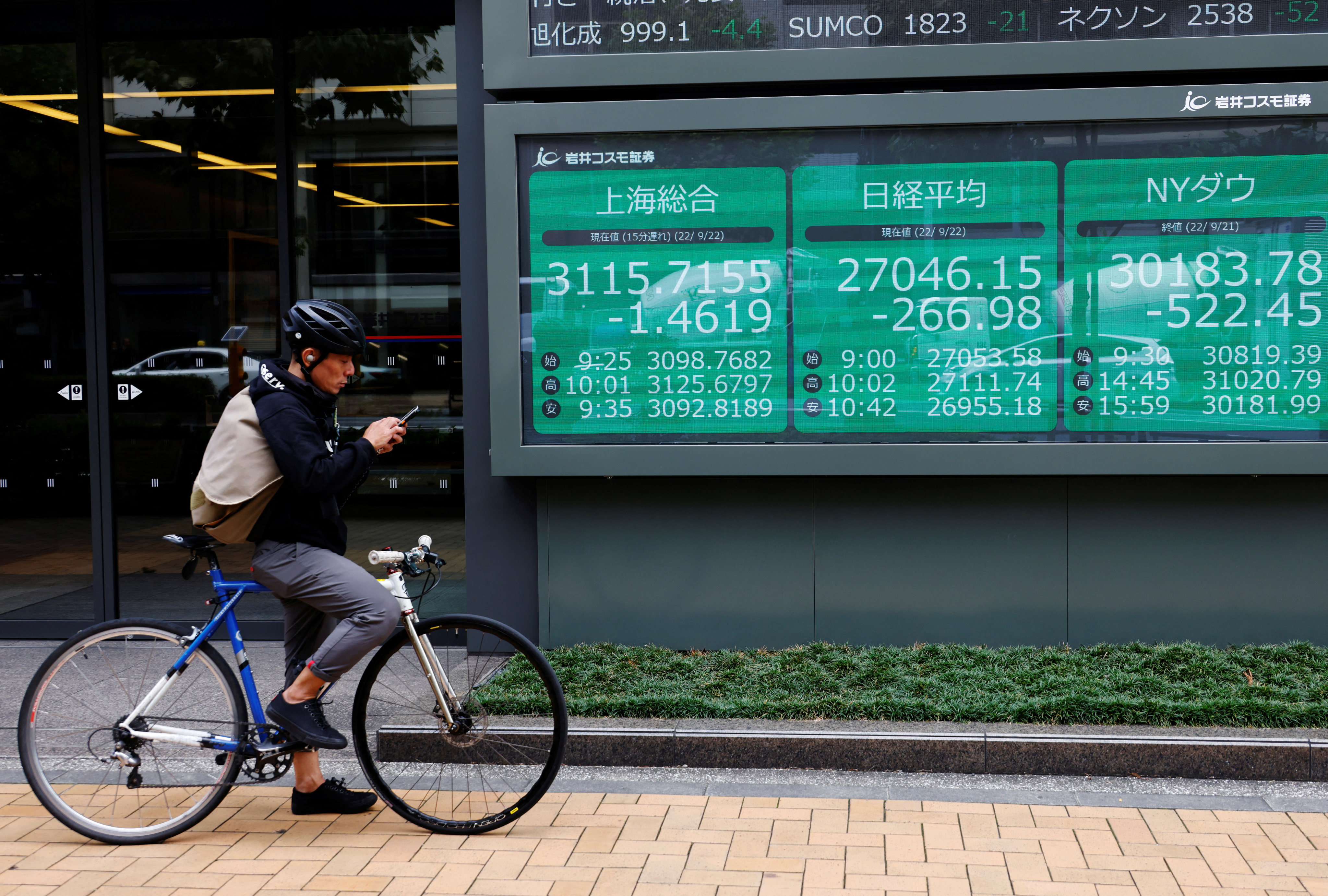 A man on a bicycle stands in front of an electronic board showing major Asian stock indices in Tokyo in September 2022. Photo: Reuters
