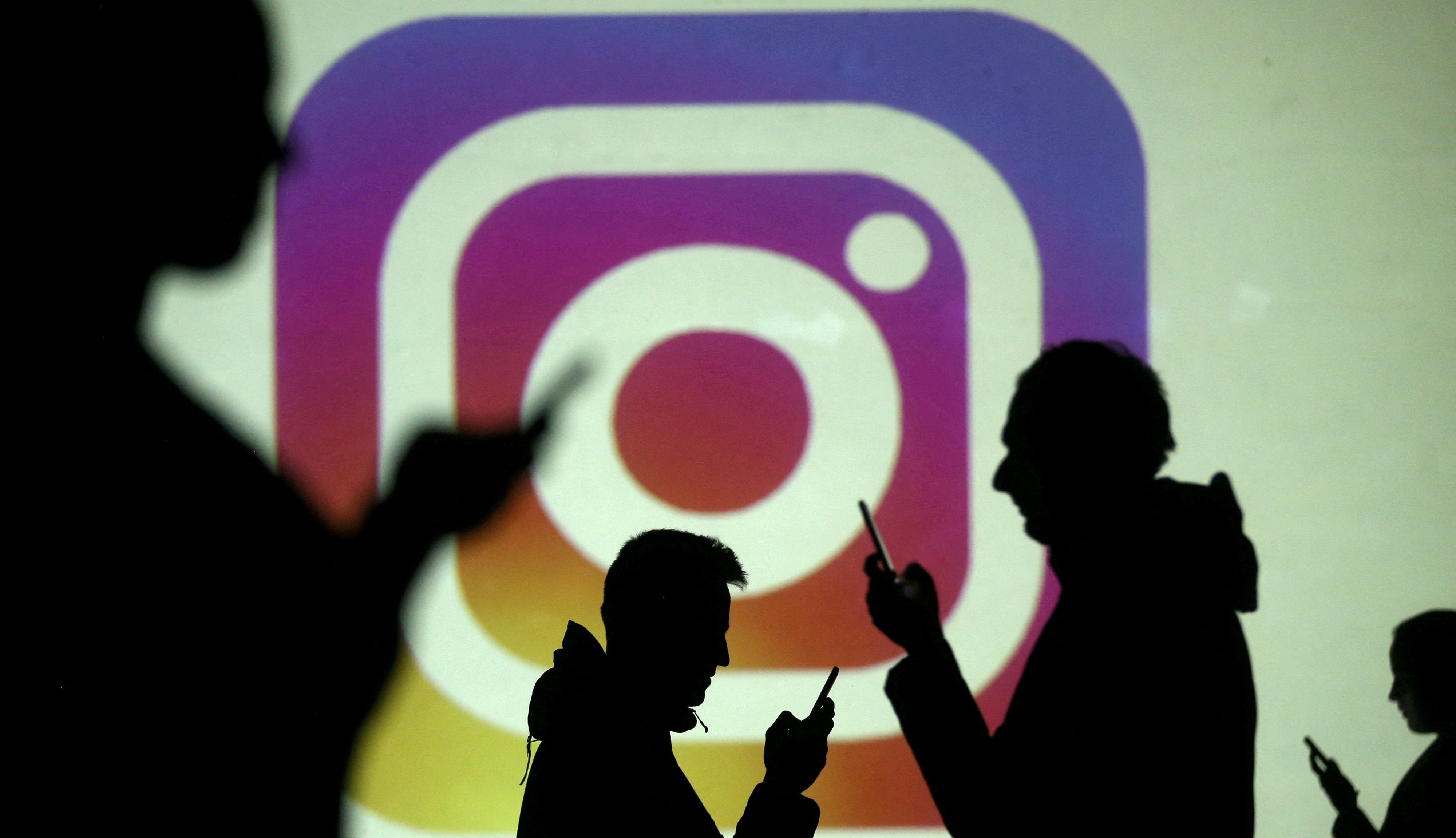 Silhouettes of smartphone users are seen next to a screen projection of the Instagram logo in this picture illustration.  Photo: Reuters
