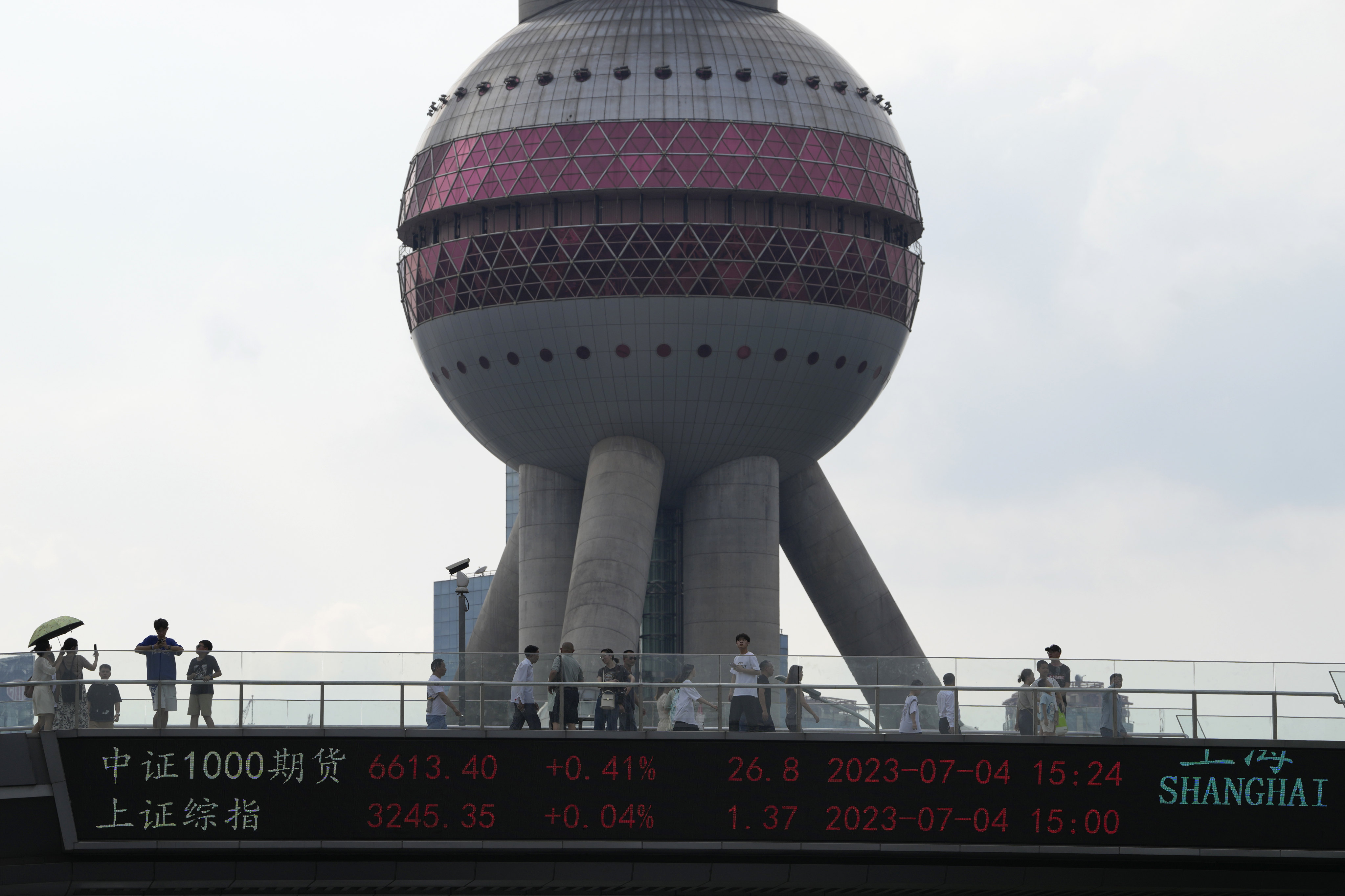 Residents pass the Oriental Pearl Tower near displays showing Chinese stock market indices in Shanghai on Tuesday. China’s sluggish recovery from the ravages of the Covid-19 pandemic has some observers worried its economy could be headed the same direction as Japan’s after the bursting of its asset bubble in the early 1990s. Photo: AP