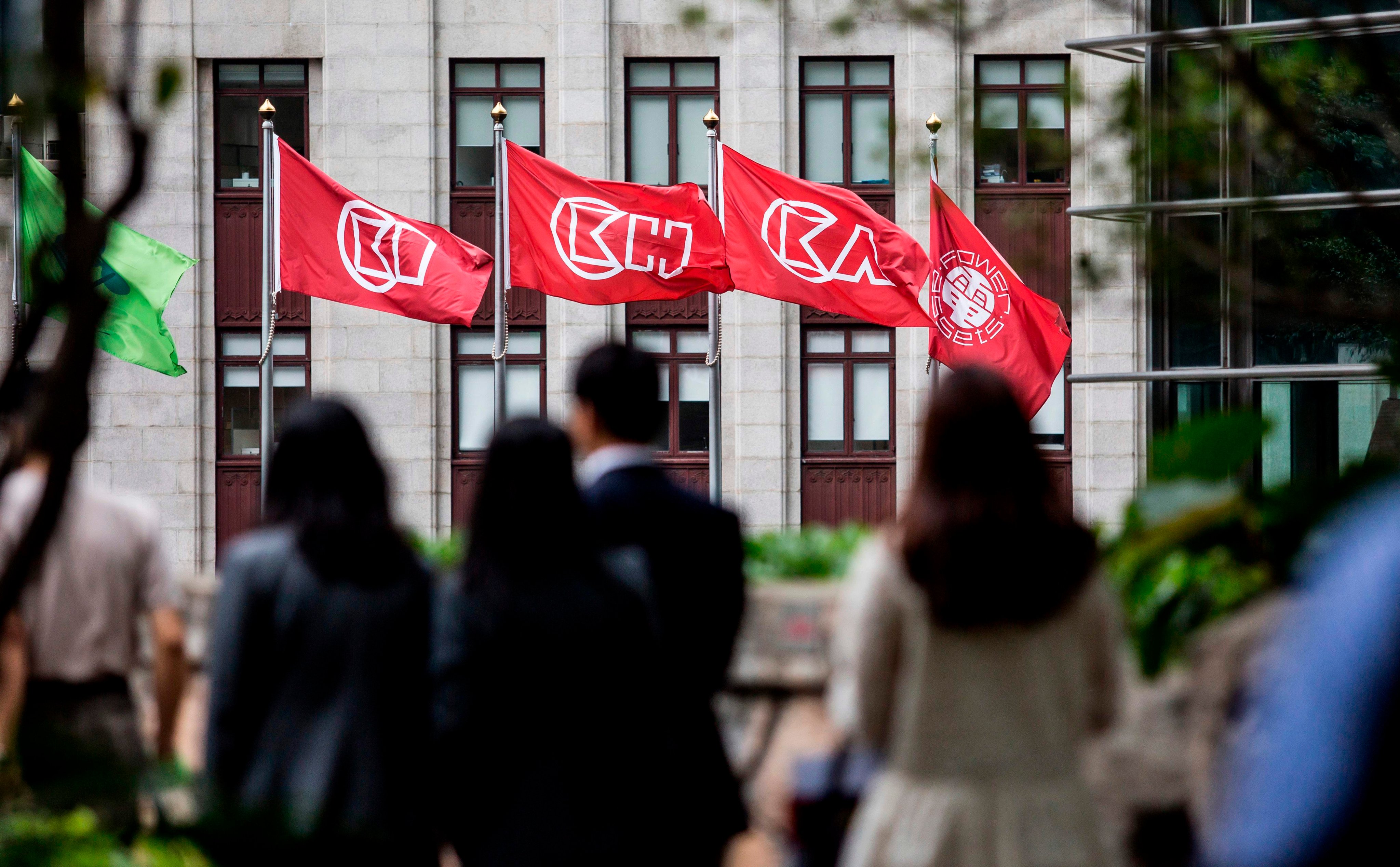 People walk near flags of CK Hutchinson Holdings outside the company’s headquarters in Hong Kong on March 21, 2019. Photo: AFP