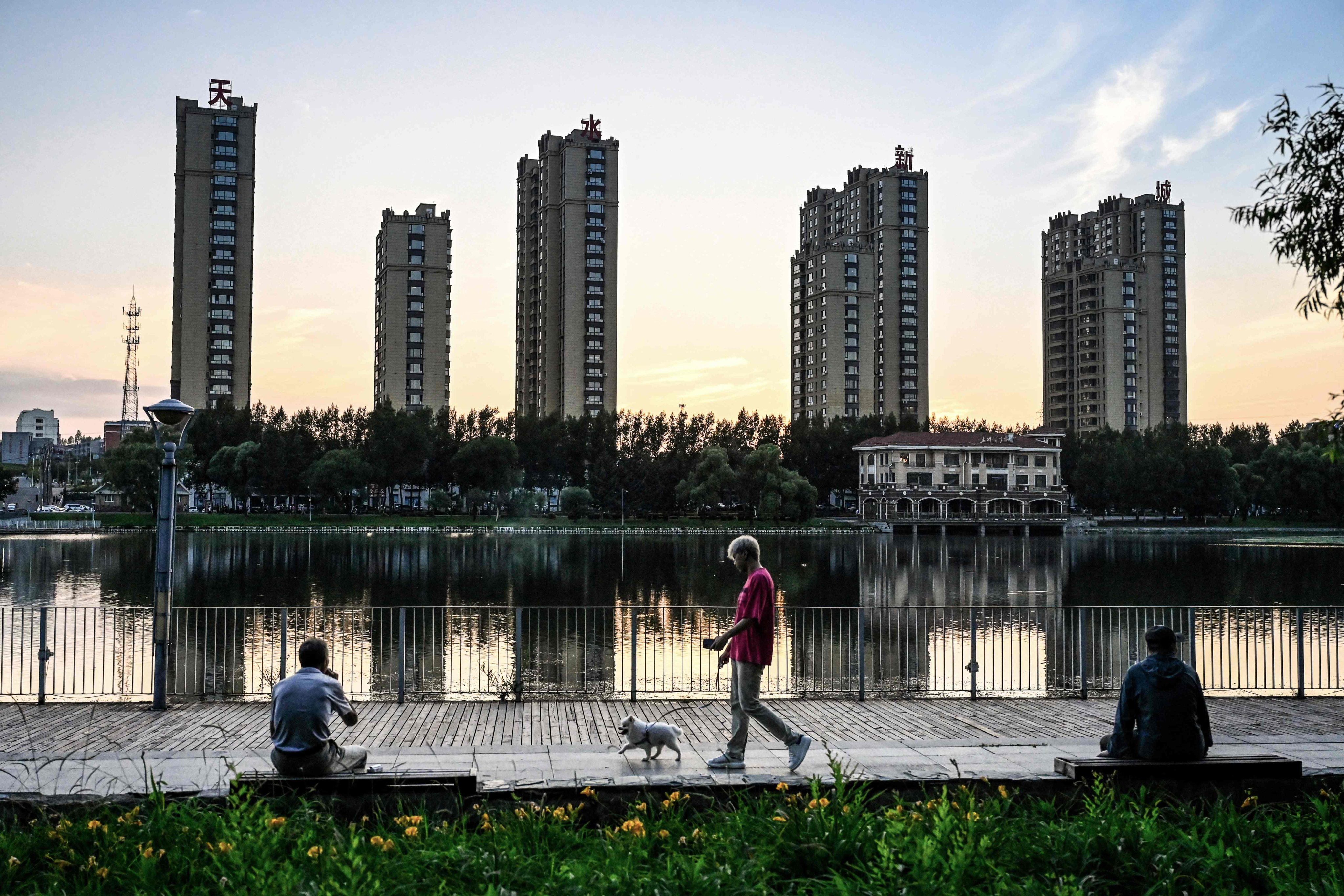 People relax by a lake near residential buildings in Hegang city in northeastern China’s Heilongjiang province on July 4. China’s real estate industry grew at lightning speed from the late 1990s, and was a major component of the country’s turbocharged economic expansion, but the market has now slumped. Photo: AFP