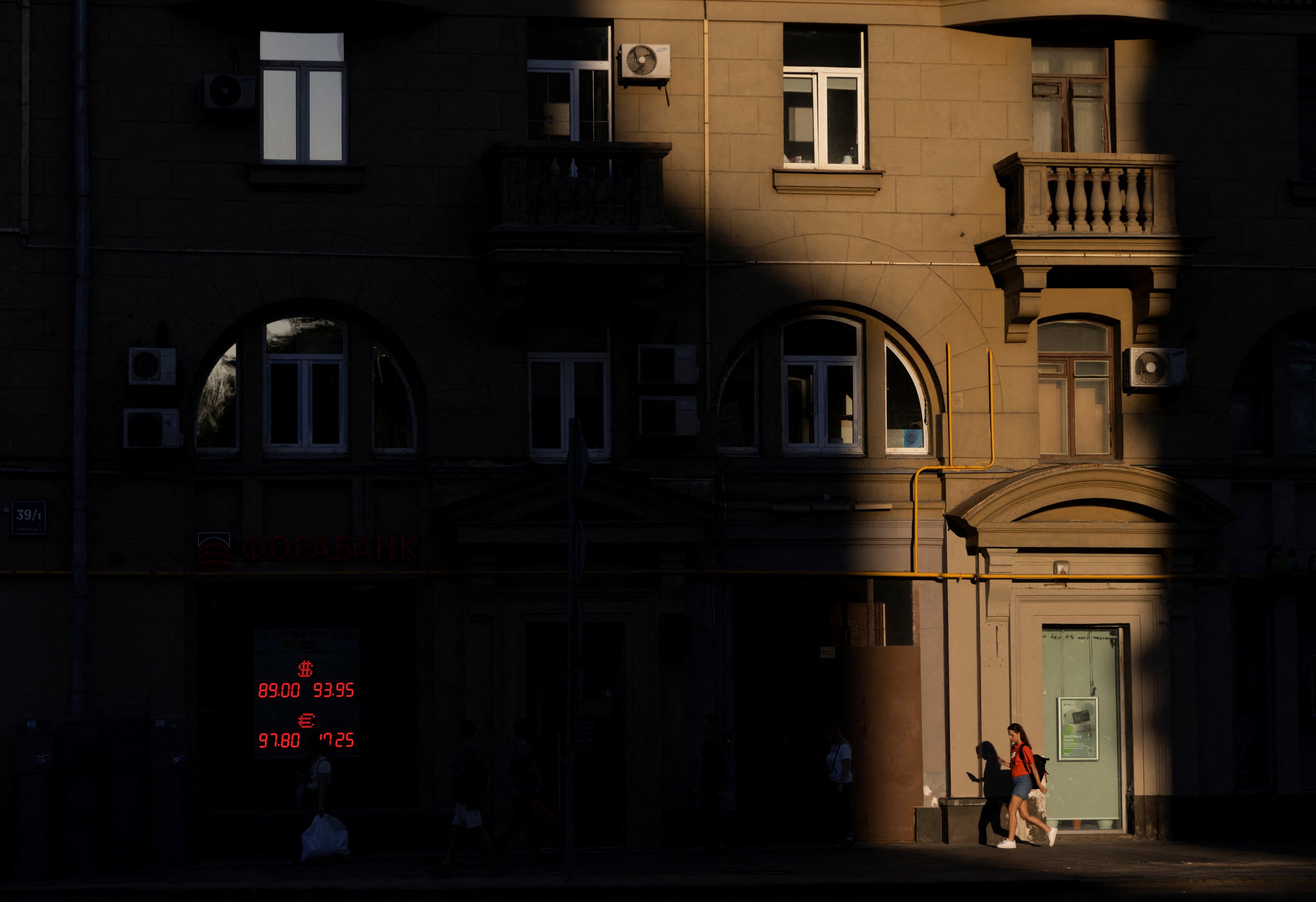 People walk next to a board showing currency exchange rates of the US dollar and euro against Russian rouble in a street in Moscow, Russia, on August 17. Photo: Reuters