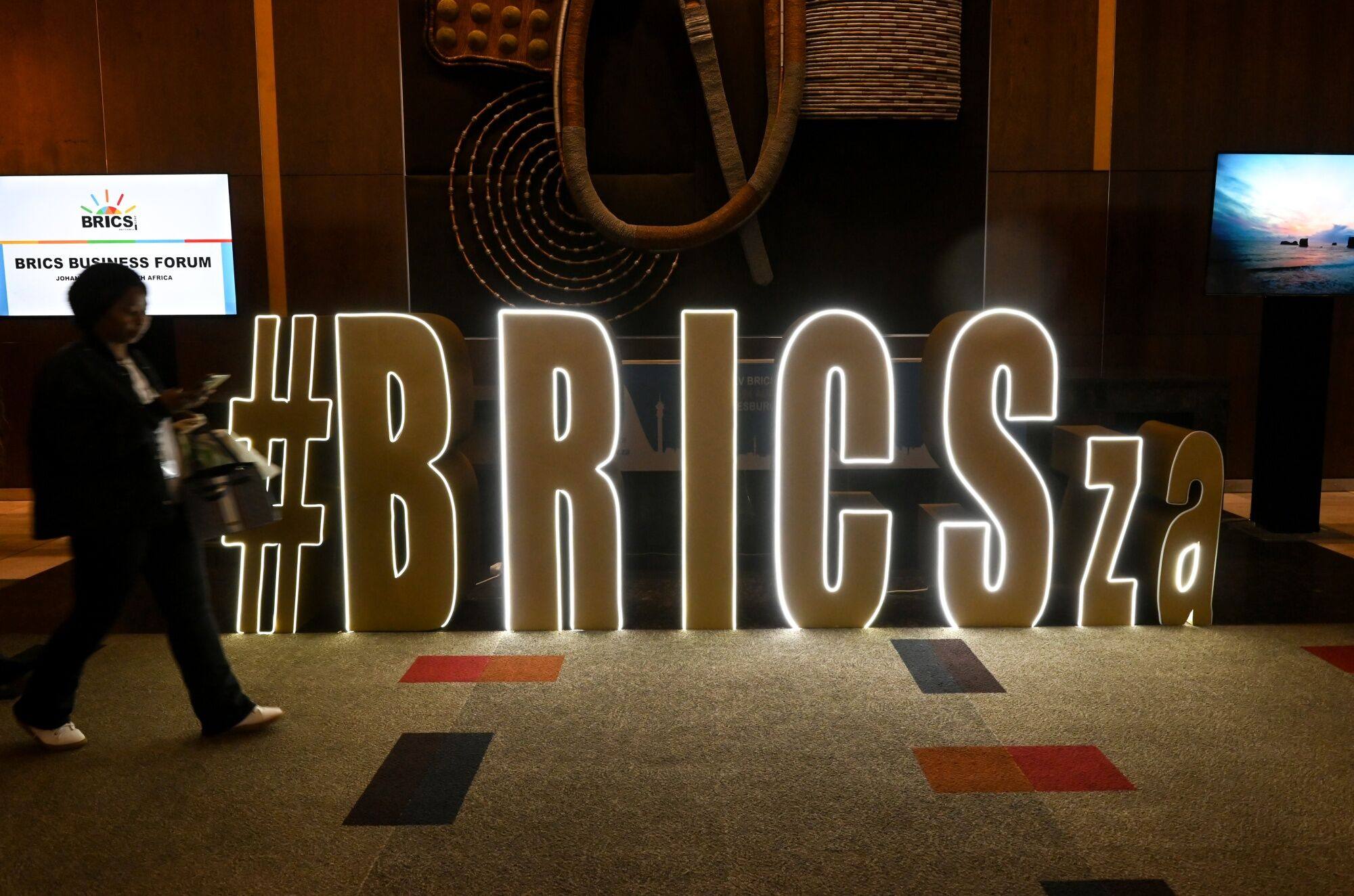 A visitor passes an illuminated sign during the Brics summit at the Sandton Convention Center in Johannesburg, South Africa, on August 22. In addition to expanding its membership, a primary focus of the grouping has been developing alternatives to using the US dollar and increasing the use of local currencies in trade and investment. Photo: Bloomberg