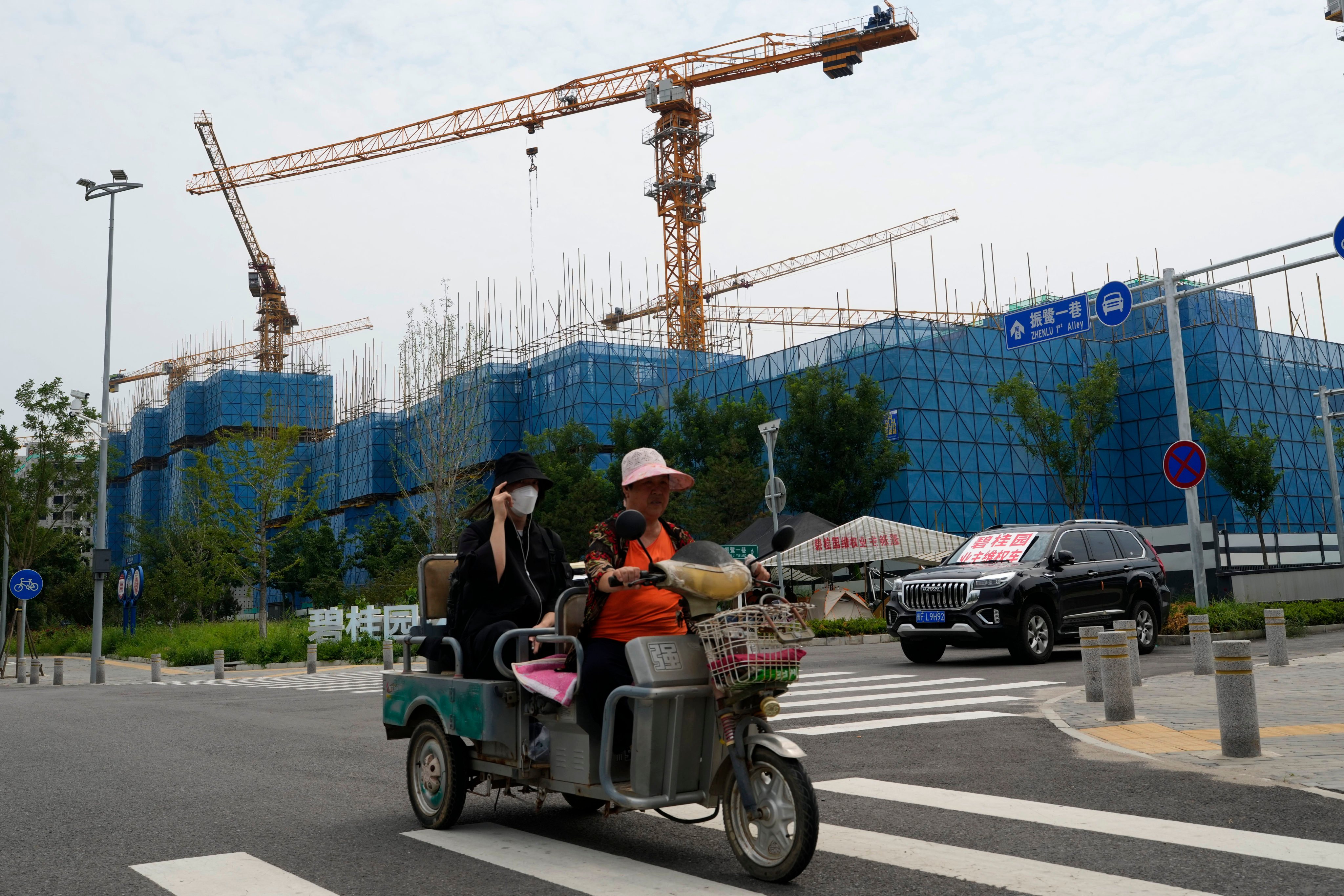 Residents on a tricycle ride past the Country Garden One World City project under construction in Beijing, August 17, 2023. Photo: AP