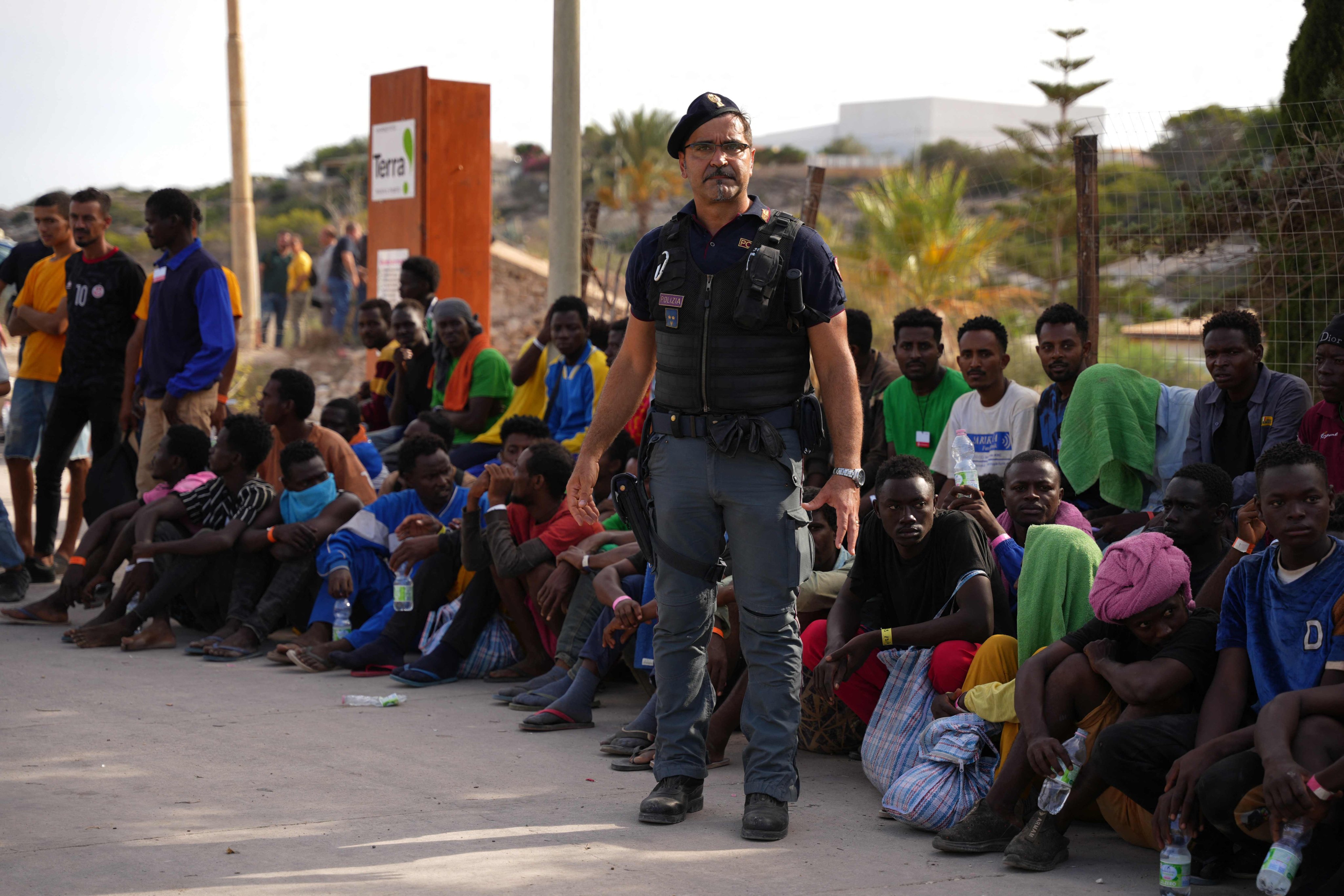 An Italian policeman stands in front of migrants sitting in the harbour of the Italian island of Lampedusa on Saturday. Photo: AFP
