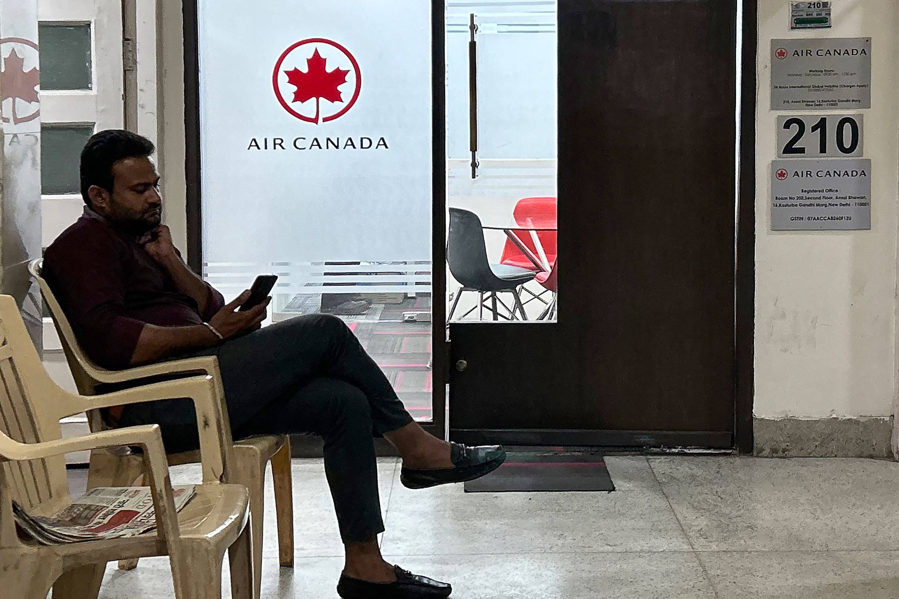 A man checks his mobile as he sits outside an Air Canada regional office in New Delhi on September 20, 2023. Photo: AFP
