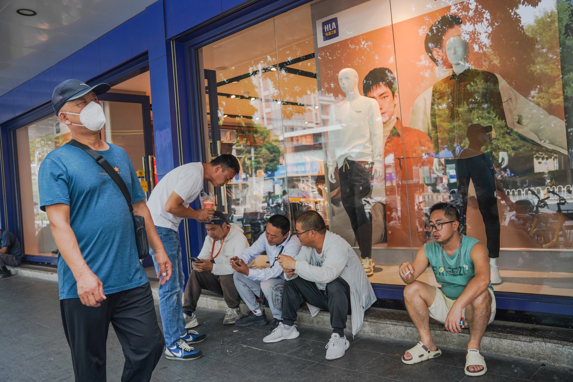 People sit beside a clothing shop in Beijing on September 7. China’s economic downturn and general uncertainty about the future have led to more savvy spending. Photo: EPA-EFE