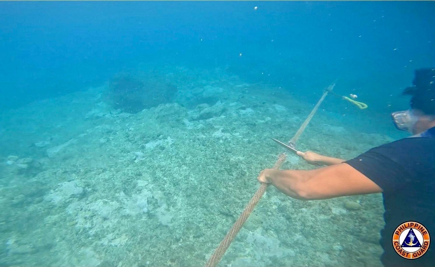 A photo released by the Philippine Coast Guard on Wednesday shows one of its members cutting a rope attached to a floating barrier blocking the entrance to Scarborough Shoal on September 21. Photo: EPA-EFE/Philippine Coast Guard