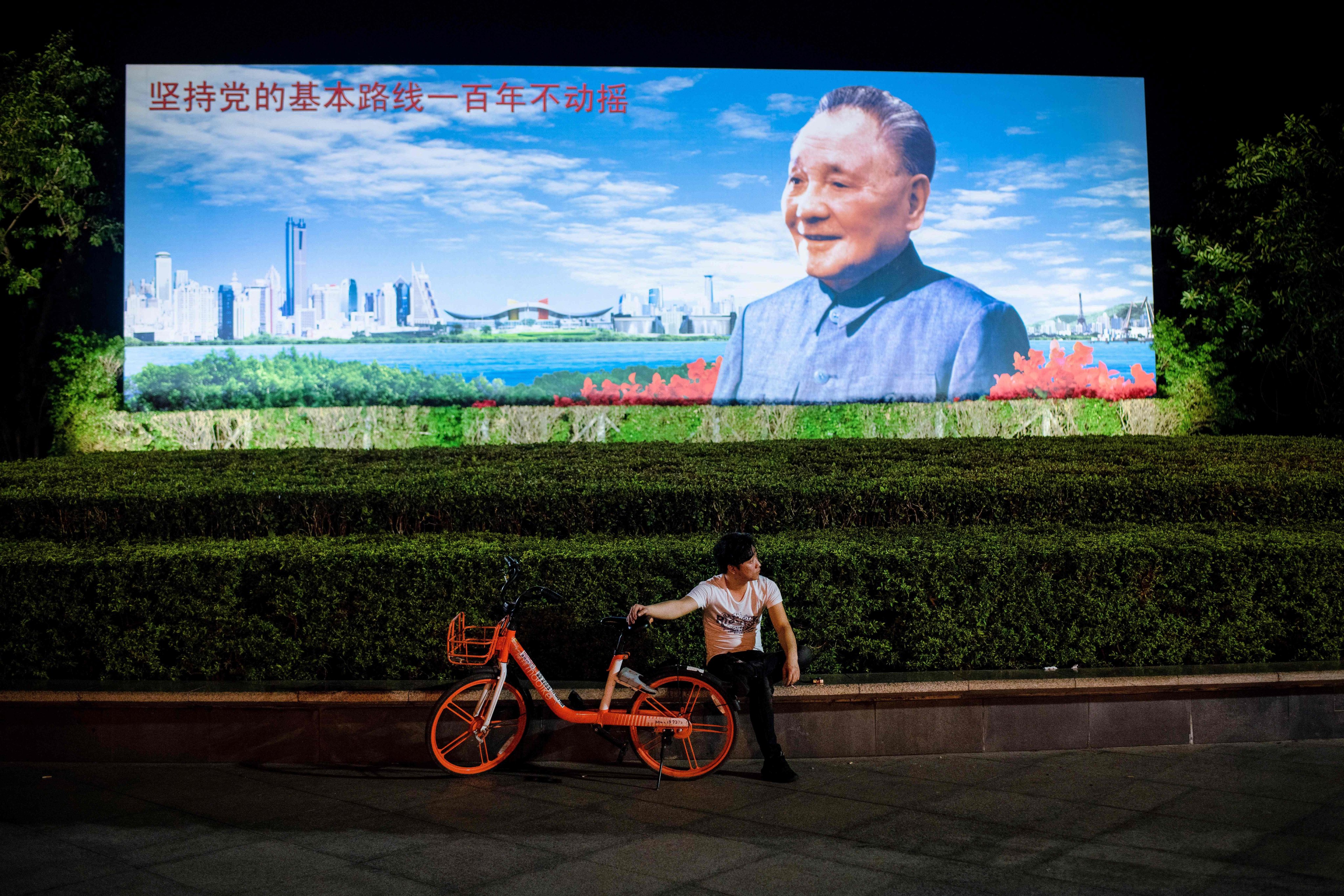 A man with a bike-share rental sitting in front of a poster of former Chinese leader Deng Xiaoping in Shenzhen on November 8, 2018. Photo: AFP